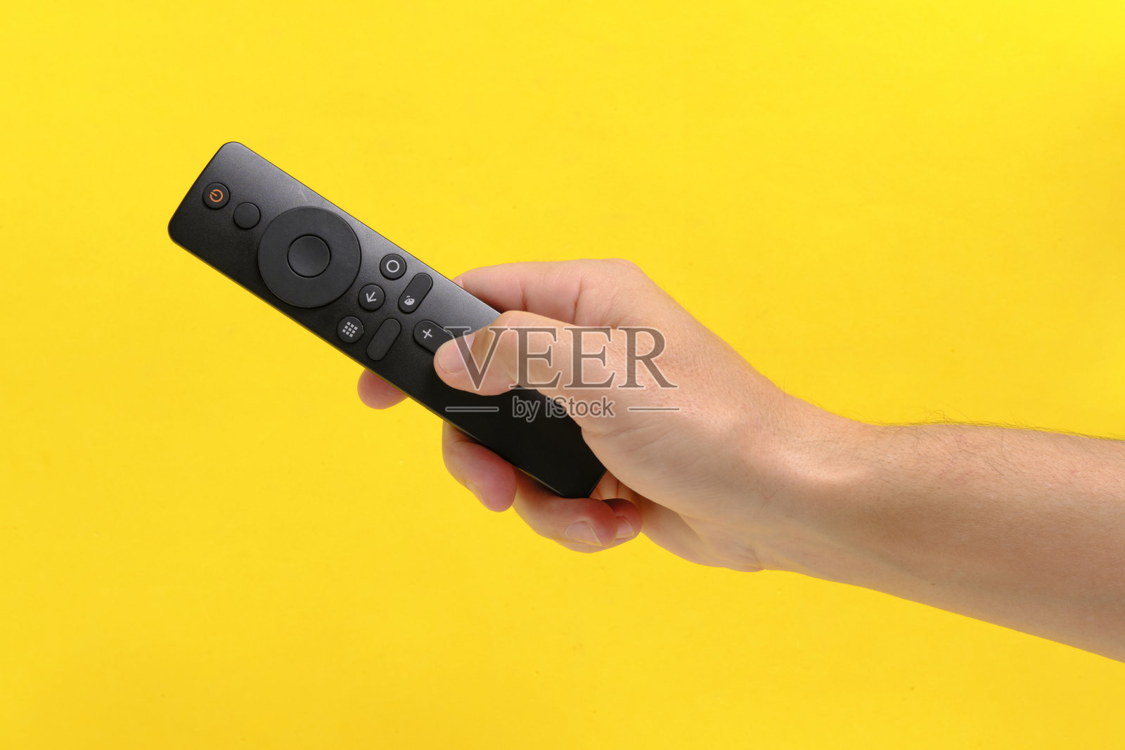 手黄色背景持有电视遥控器按按钮与手指。照片摄影图片