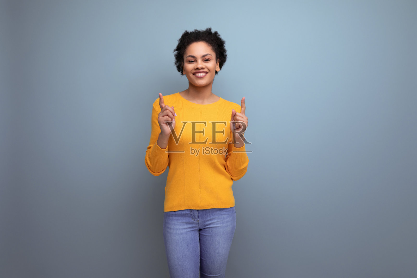 一位身穿黄色毛衣，有着一头黑色卷发的年轻西班牙裔女子举起食指照片摄影图片