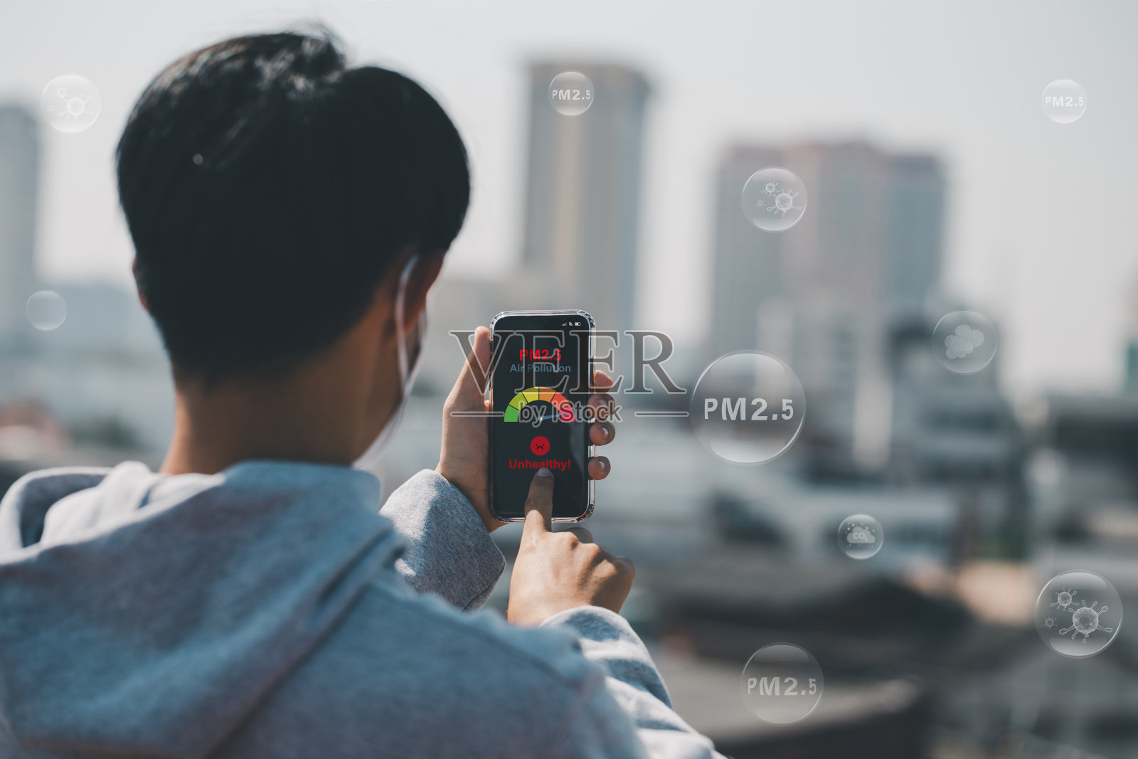 一名亚洲男子正在用智能手机扫描雾霾城市上空的天气。从细颗粒物看恶劣天气下的建筑物。城市空气污染与不健康概念。pm2.5照片摄影图片