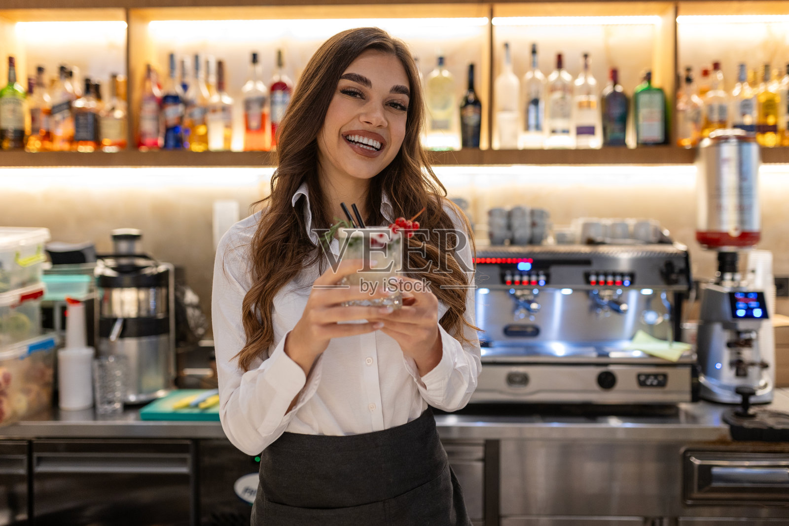 快乐的年轻女酒保，穿着时髦的衣服，站在柜台前，看着镜头，端上冬天的莫吉托鸡尾酒照片摄影图片