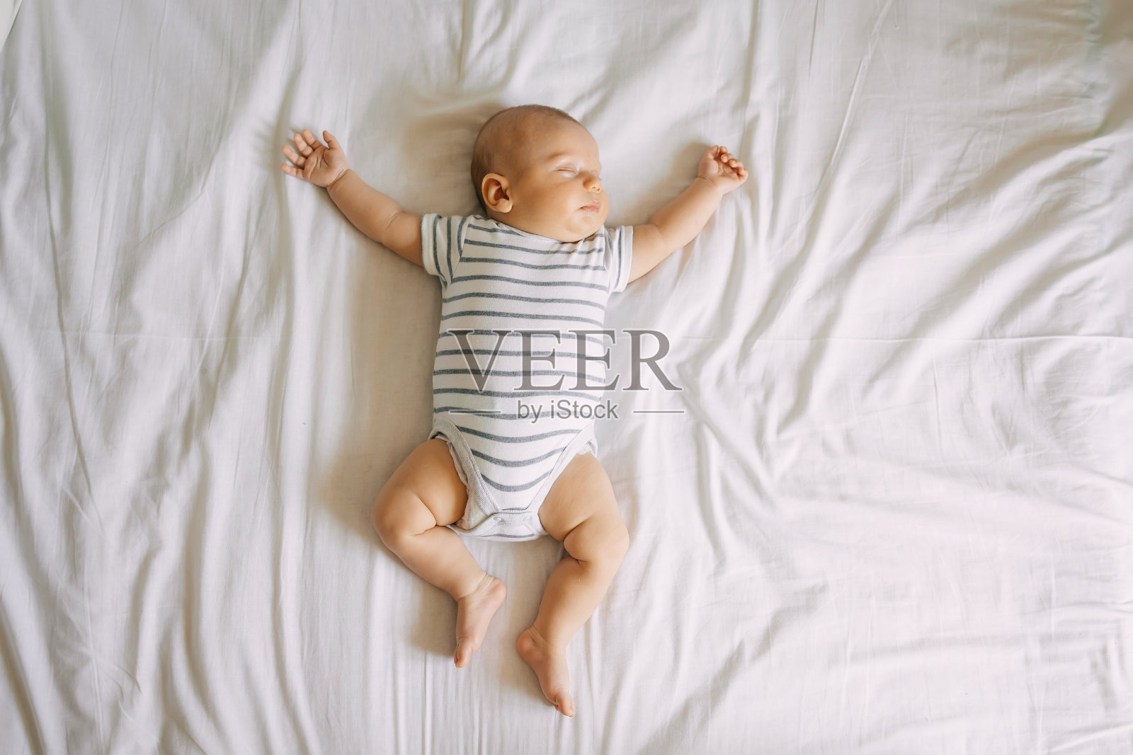 俯视图熟睡的新生婴儿躺在床上，胳膊和腿伸直。干净、清新、舒适的床单照片摄影图片