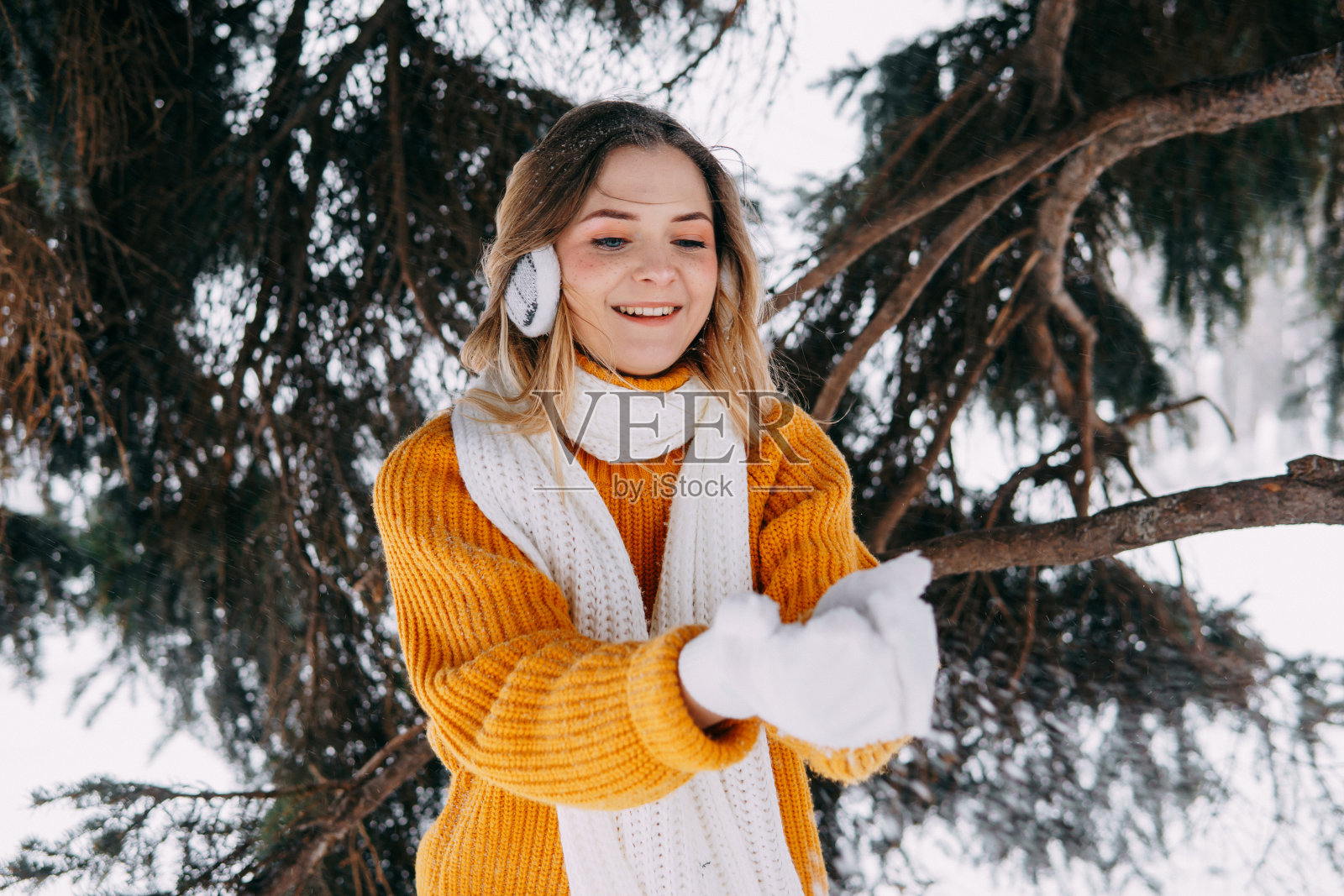 冬天在外面穿黄色毛衣的金发少女。一个十几岁的女孩穿着冬装在白雪皑皑的森林里散步照片摄影图片