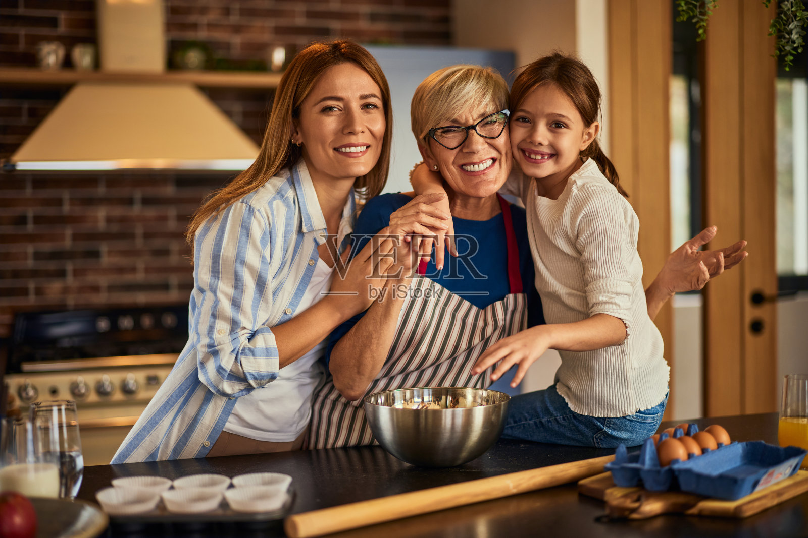 这是一幅三代同堂的肖像，奶奶、母亲和女儿在厨房里微笑着做饭。照片摄影图片