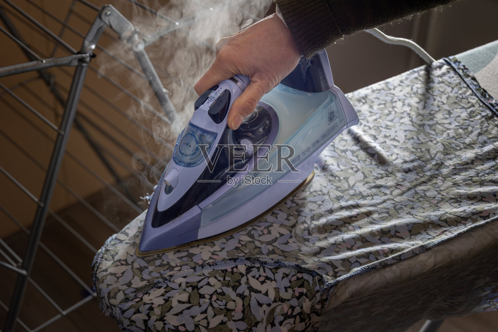 在熨烫台上用浅紫色的热蒸汽熨斗烫衣服照片摄影图片