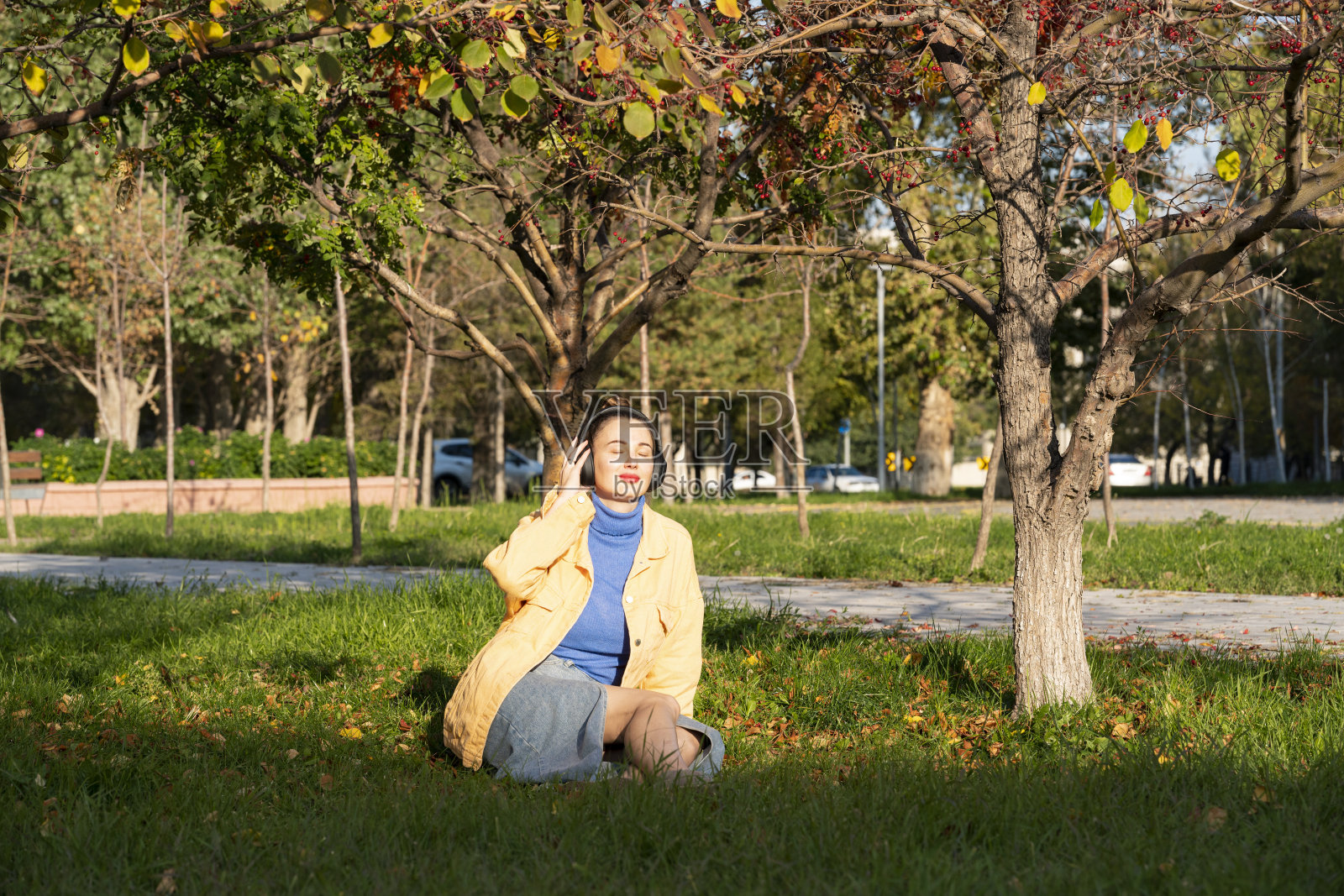 一位年轻女子坐在公园的绿草地上，戴着耳机欣赏音乐。照片摄影图片