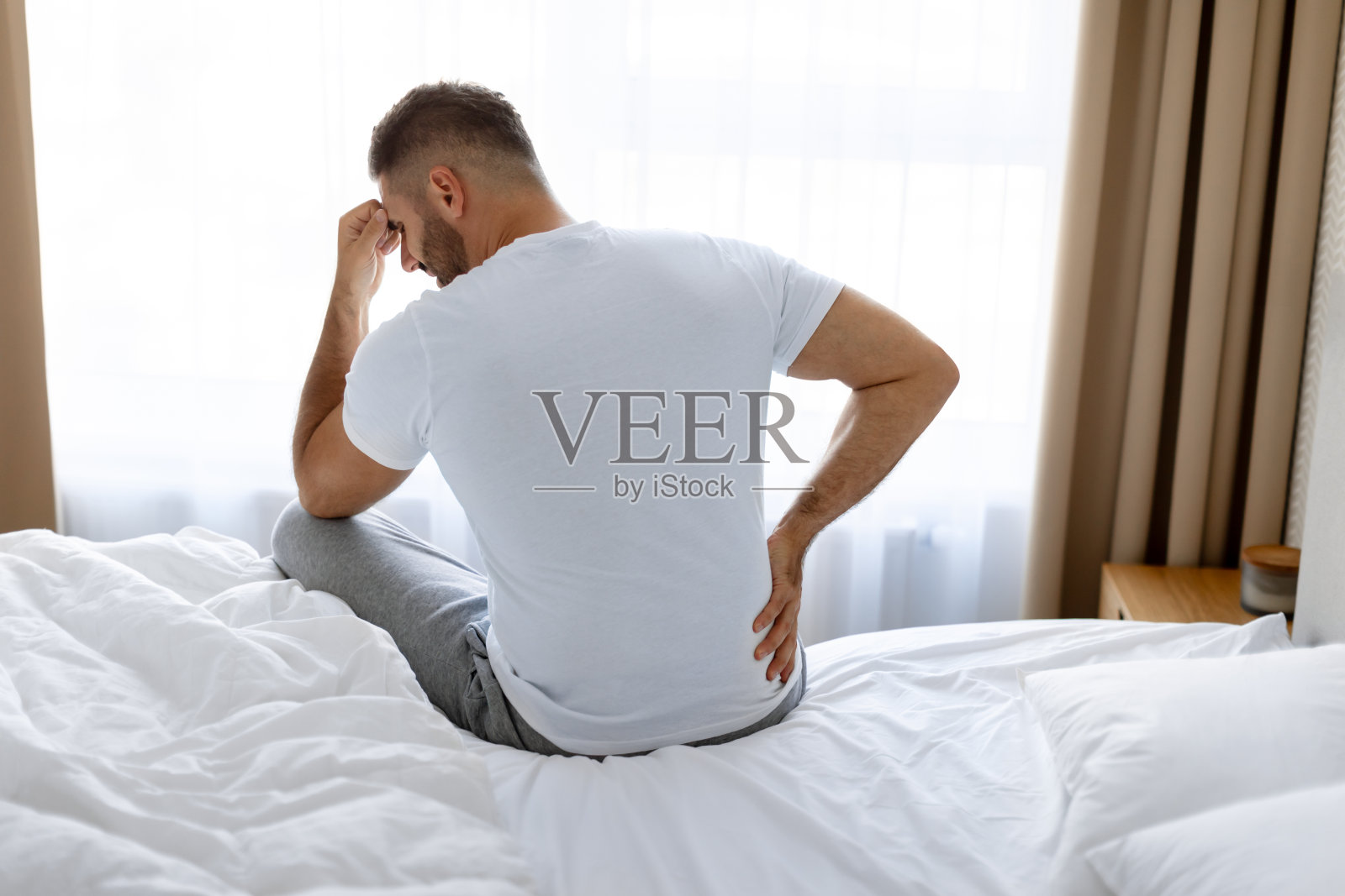 男子触摸下背部，在卧室遭受痛苦的背痛照片摄影图片