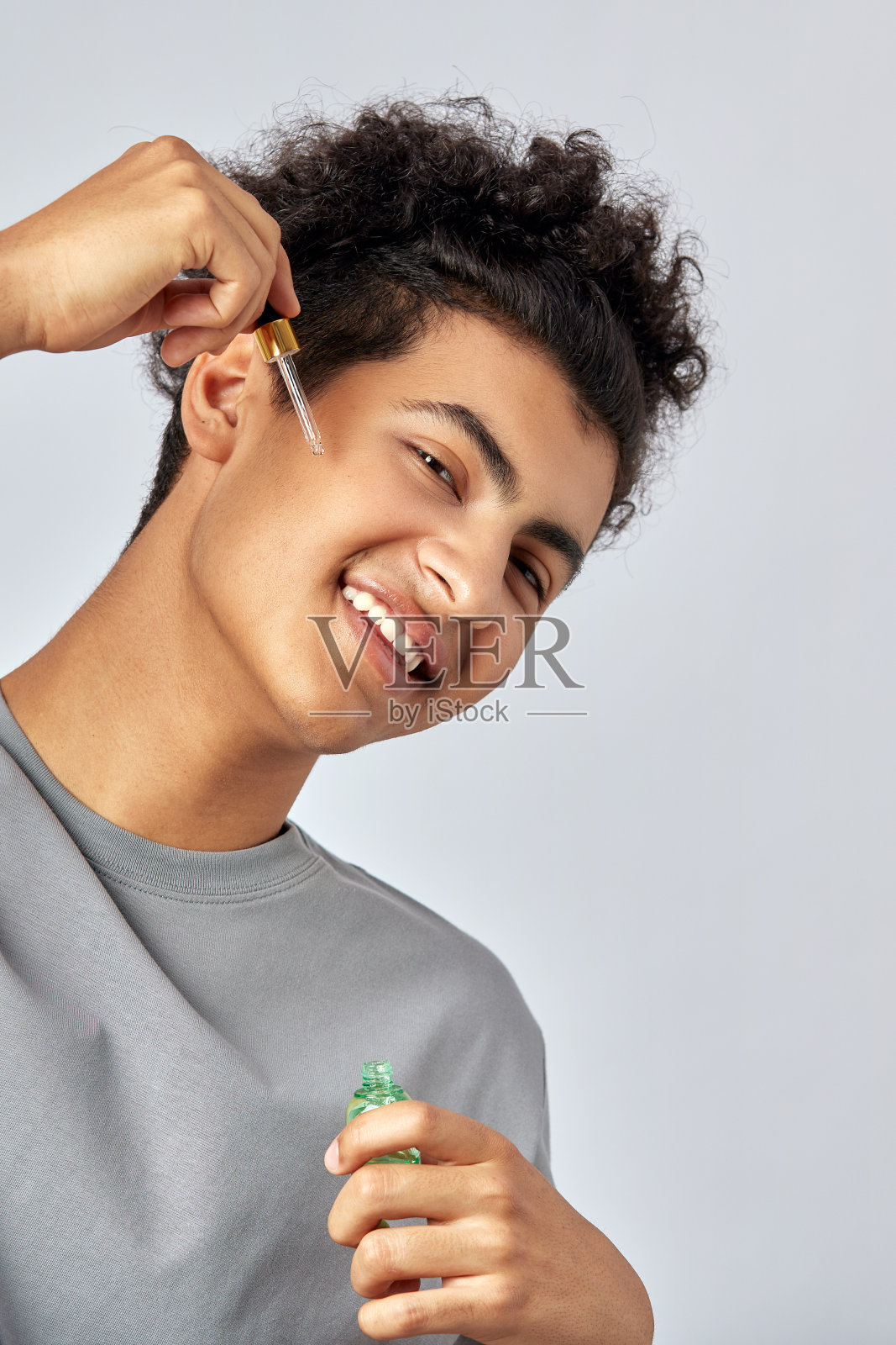 一个有着黑色卷发的年轻人正在用面部油滋润皮肤，这是一个抗衰老的护肤程序。英俊黝黑的男人呵护他的皮肤，以达到更健康和容光焕发的外观。照片摄影图片