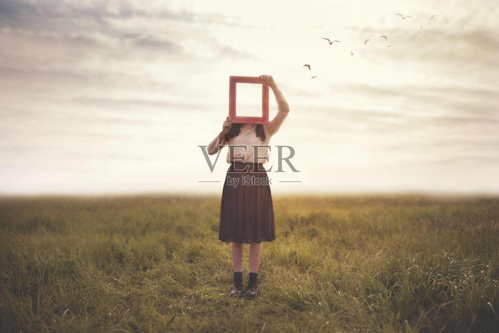 女人拿着一个空的框架，使她的脸消失，反映了天空，抽象的概念照片摄影图片