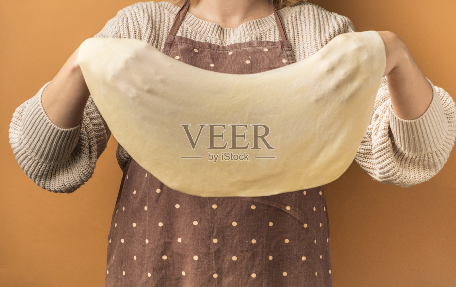 糕点师在传统的围裙上拿着生的菲罗油酥皮，在米色温暖的背景上，自制的薄菲罗油酥皮用于烘焙派和蛋糕照片摄影图片