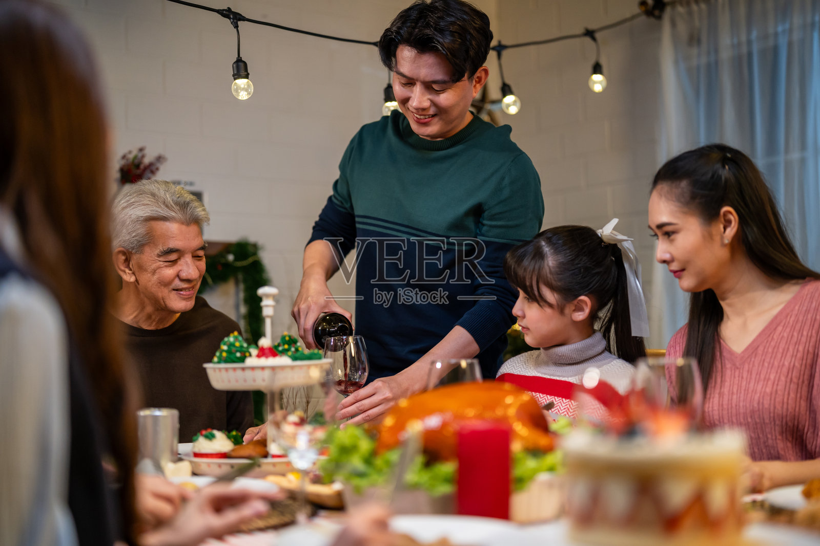 亚洲可爱的家庭在家里一起庆祝圣诞派对。迷人的父母和亲戚们在家里的餐桌上吃着感恩节大餐，庆祝圣诞前夜的节日。照片摄影图片