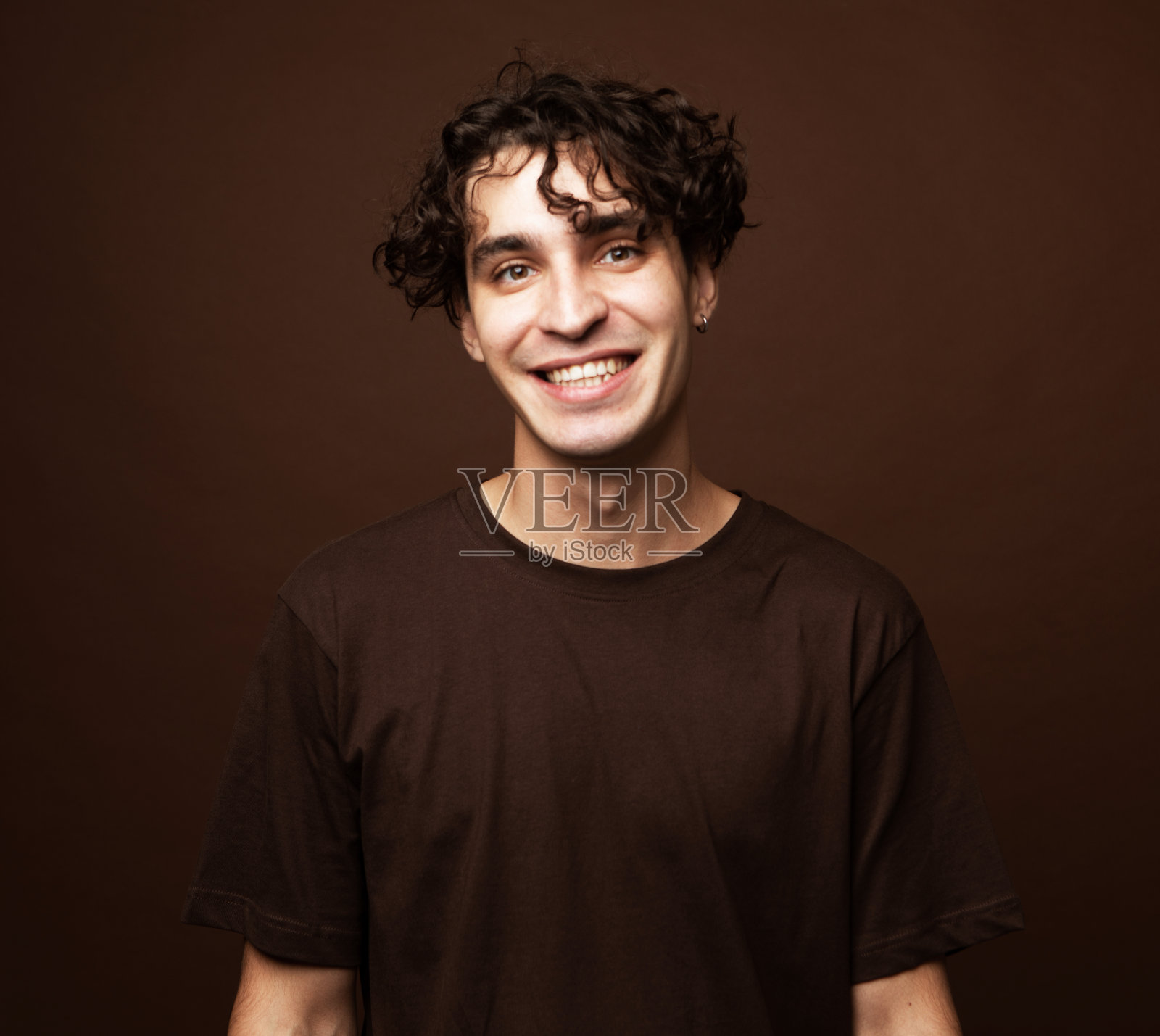 在棕色背景上，快乐微笑的男人看着相机的肖像照片摄影图片