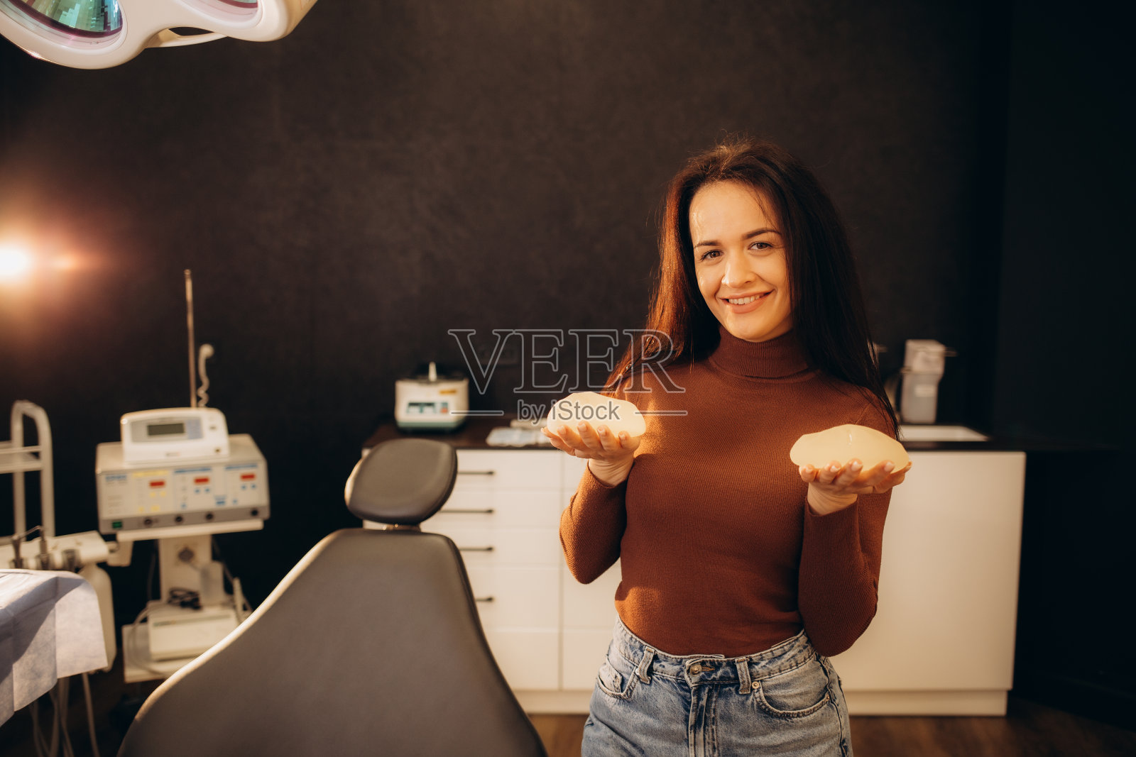 诊所访问和女性隆胸选择。特写，医生戴着手套的手拿着女性乳房植入物。年轻女子手里拿着女性乳房硅胶植入物。照片摄影图片