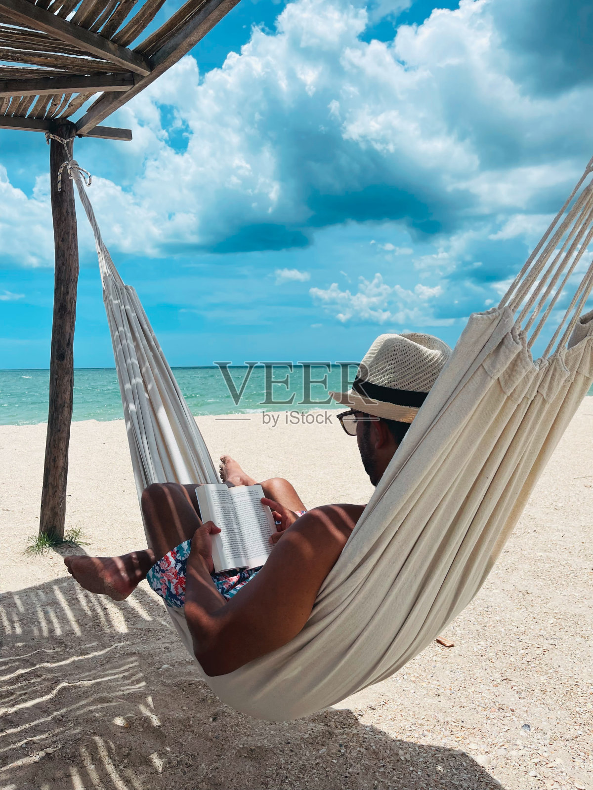 哥伦比亚瓜希拉，一名男子在海滩上的吊床上看书照片摄影图片