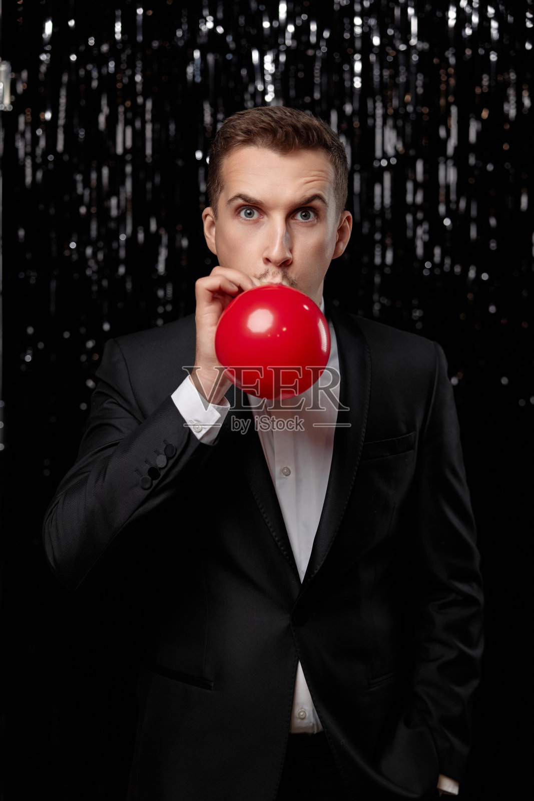 穿黑夹克的白人男子正在吹红色气球照片摄影图片