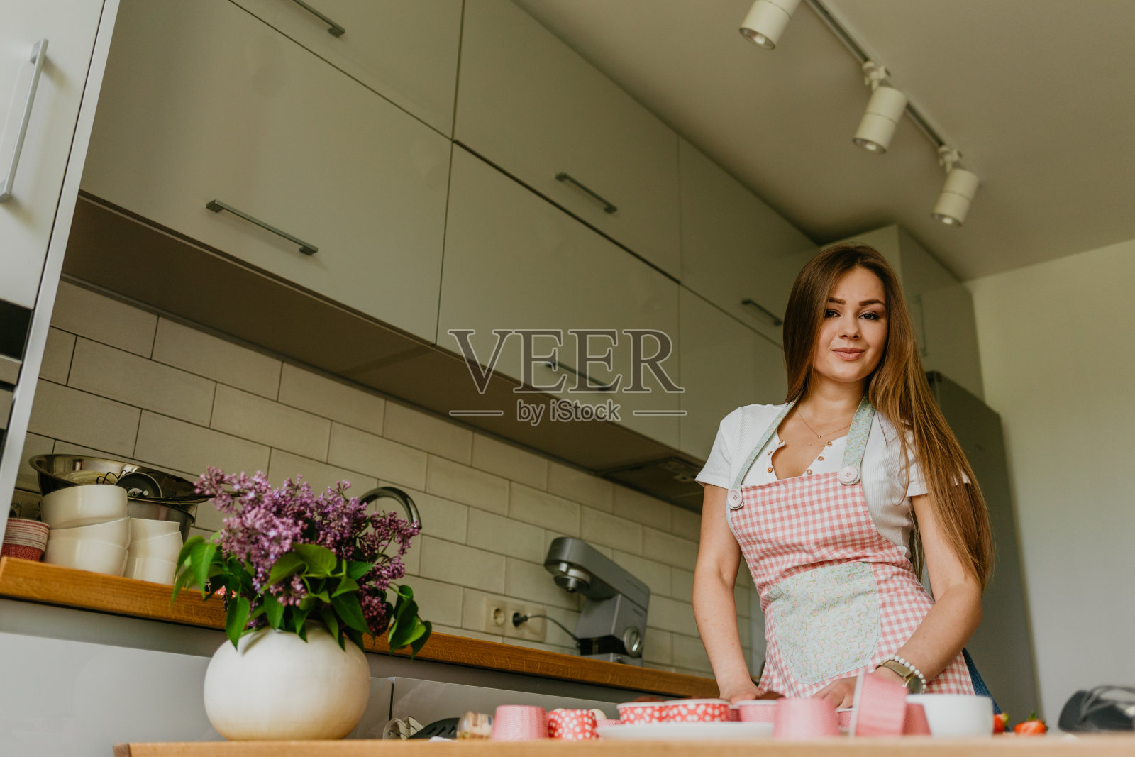 友善微笑的女性专业糖果师用糕点袋给纸杯蛋糕浇上奶油的照片。看着镜头。在室内的形象。做奶油蛋糕的女糕点师照片摄影图片