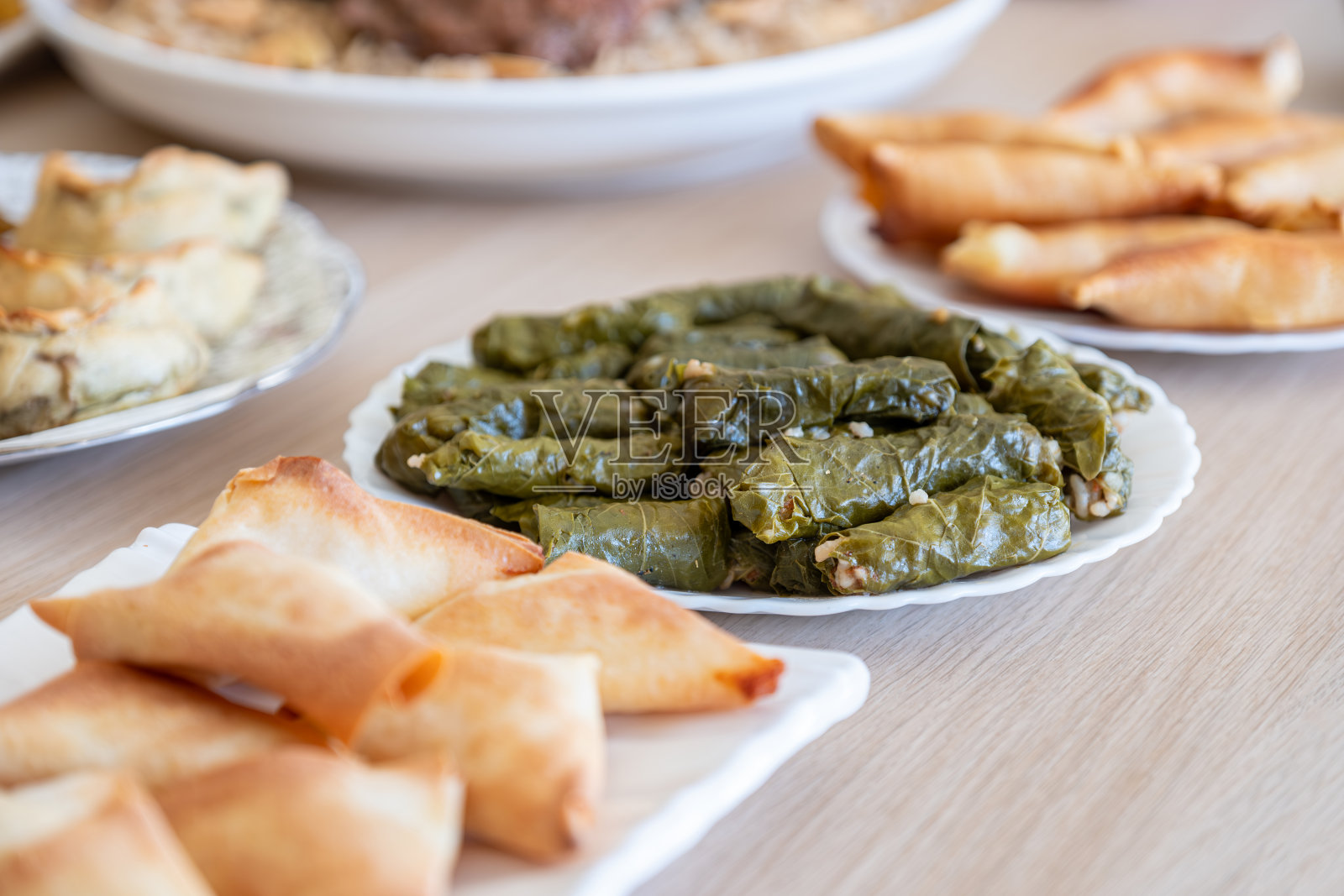 木桌上的葡萄卷拼盘，搭配 sambousek 和 qatayef照片摄影图片