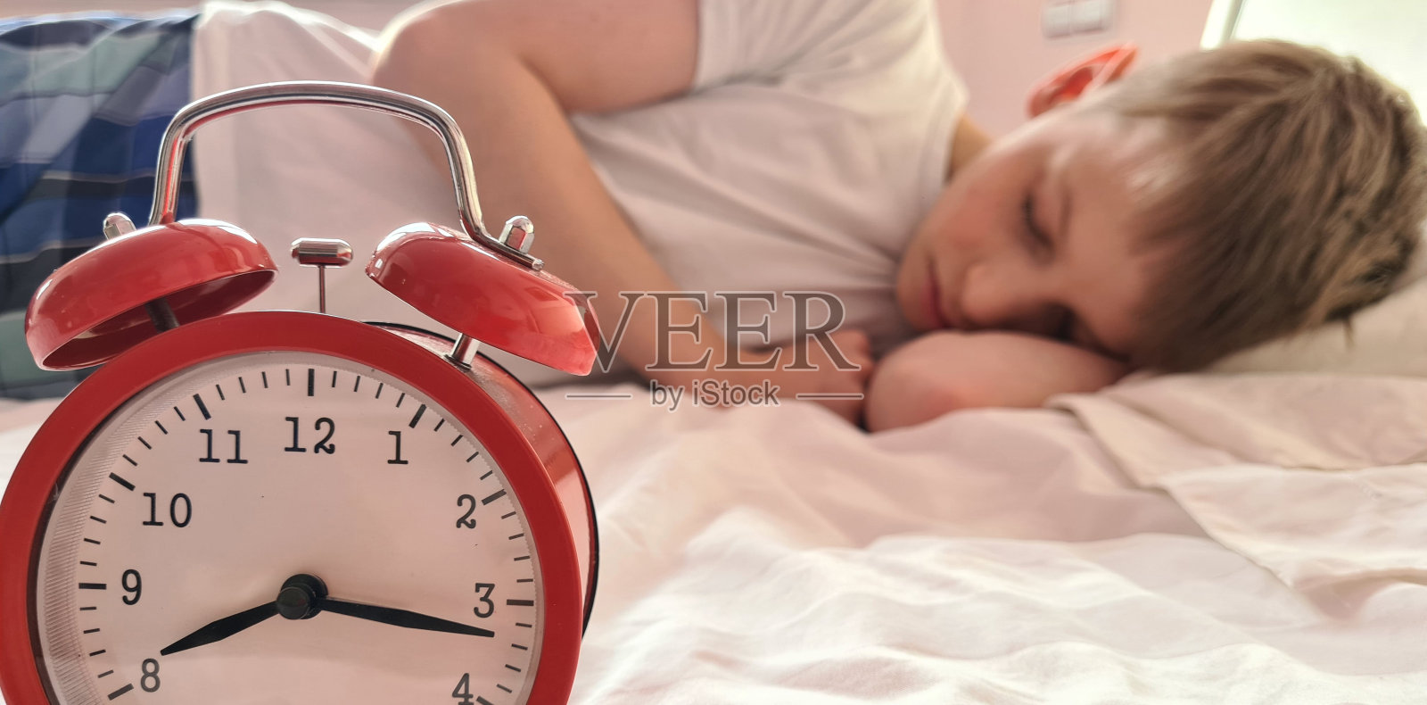 可爱的宝宝带着闹钟安静地睡在床上照片摄影图片