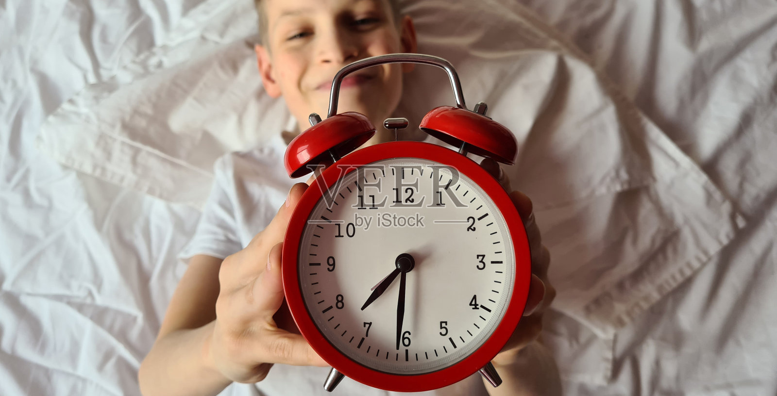 微笑的男孩在床上有一个闹钟照片摄影图片