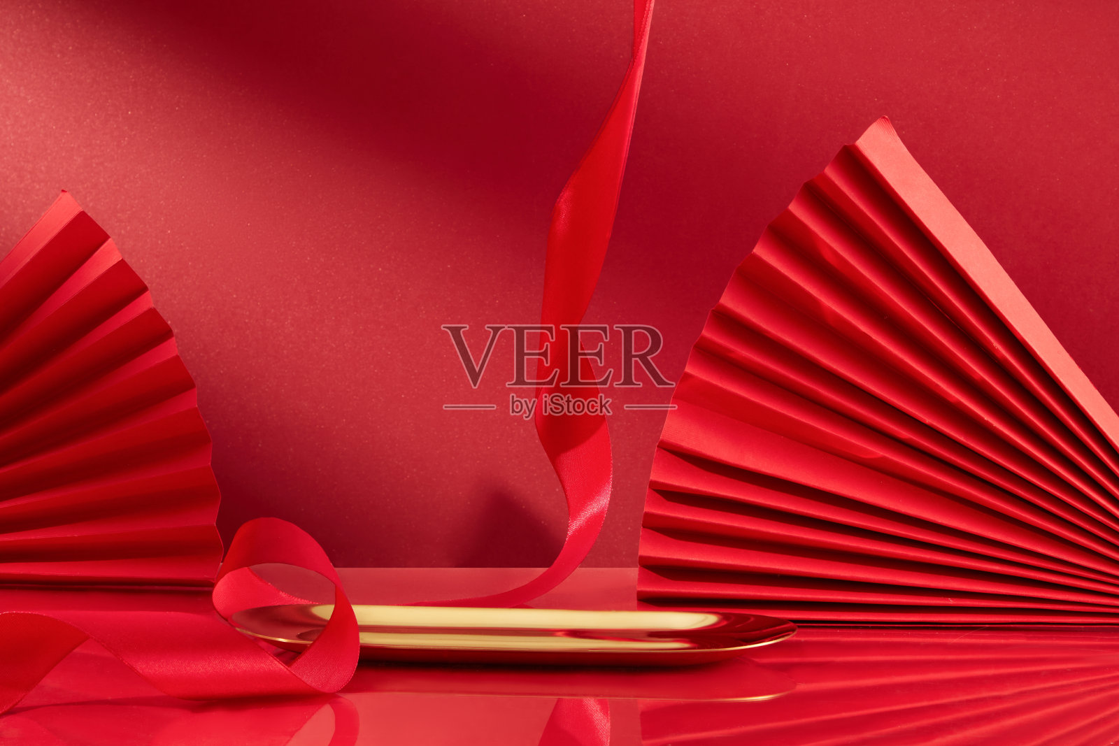 两个纸扇，一条缎带和一个金属托盘显示在红色背景上。春节期间推出的产品广告位。前视图。照片摄影图片