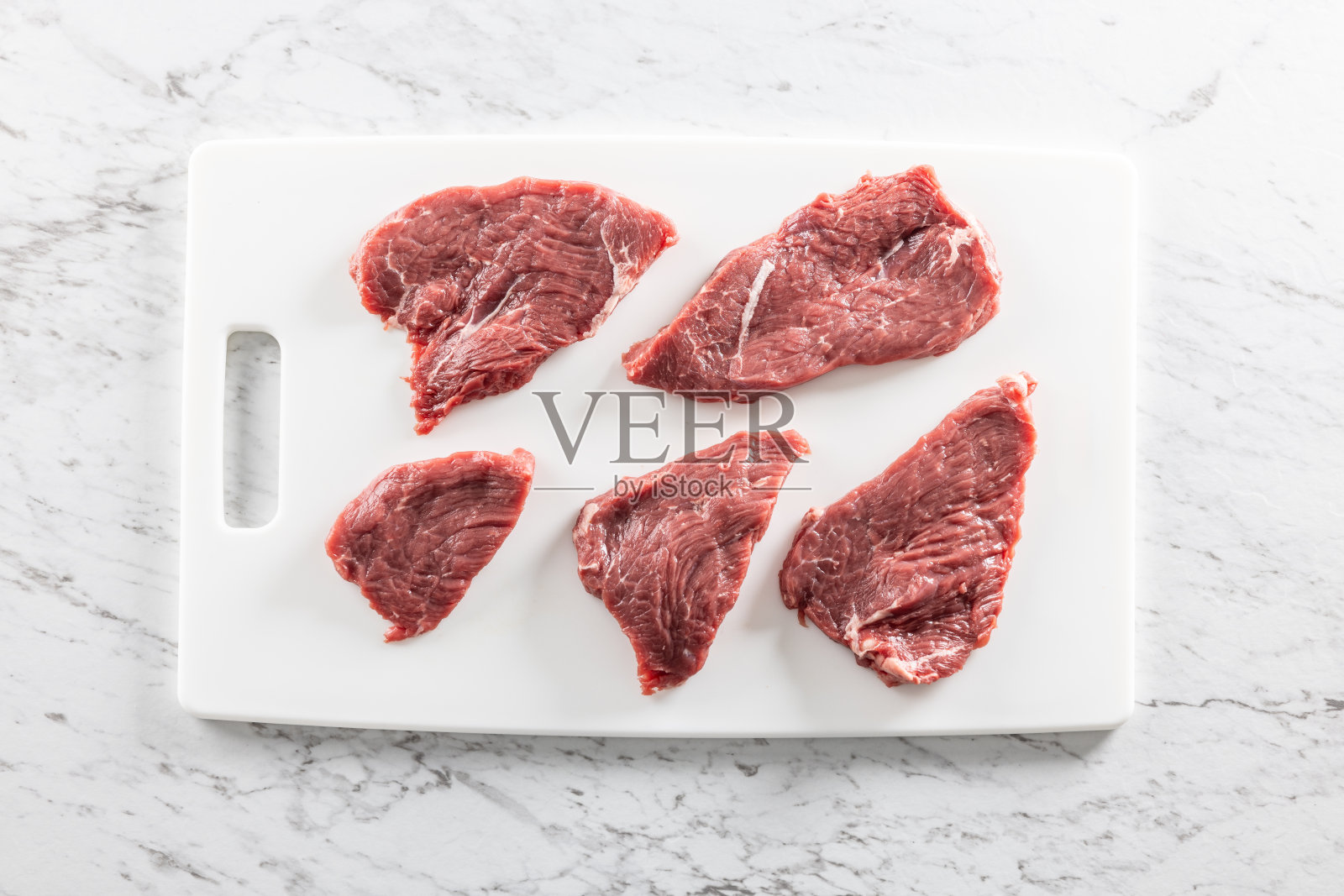 生的新鲜牛肉在白色砧板上切成牛排。俯视图。照片摄影图片