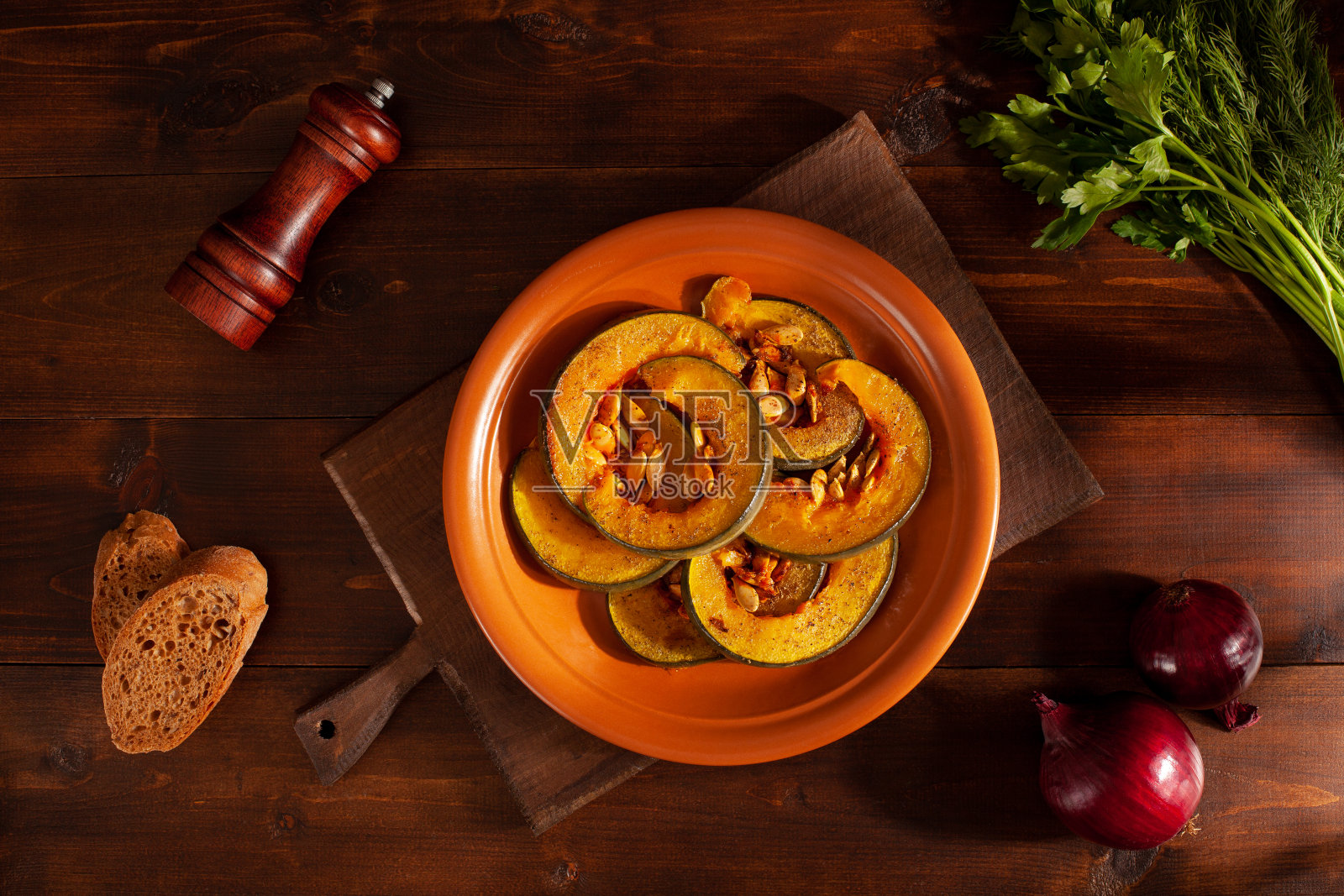 深色木桌上有烤南瓜、香草和洋葱照片摄影图片