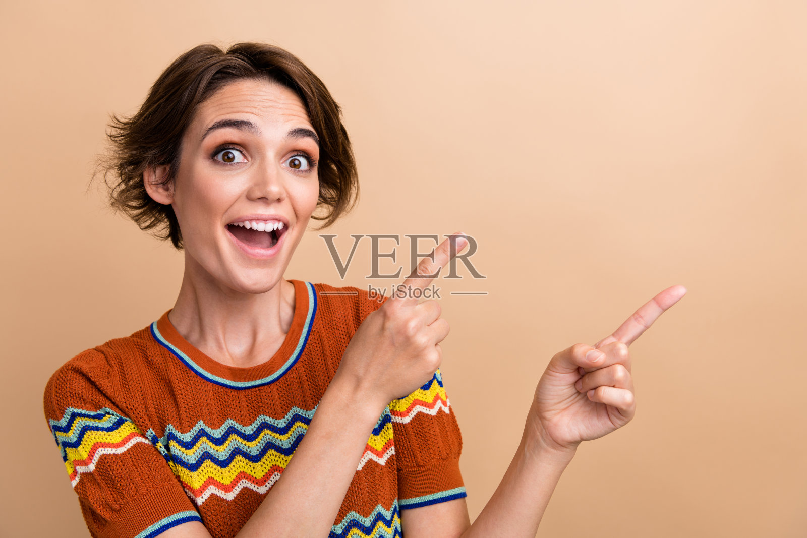 照片中惊讶的开朗的漂亮女孩张开嘴直接手指空白的空间和孤立的米色背景照片摄影图片