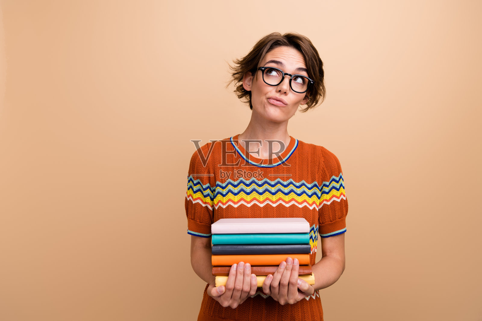 头脑聪明的女士拿着一堆书的照片，在米色的背景上看起来空空荡荡的头脑风暴照片摄影图片