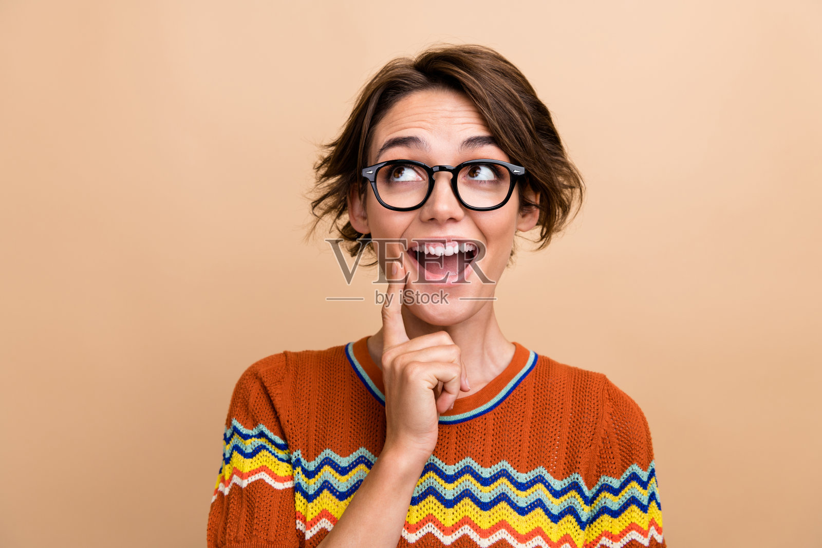 印象深刻的开朗聪明的女孩张开嘴，手指触摸下巴看起来空白空间孤立在米色背景照片摄影图片