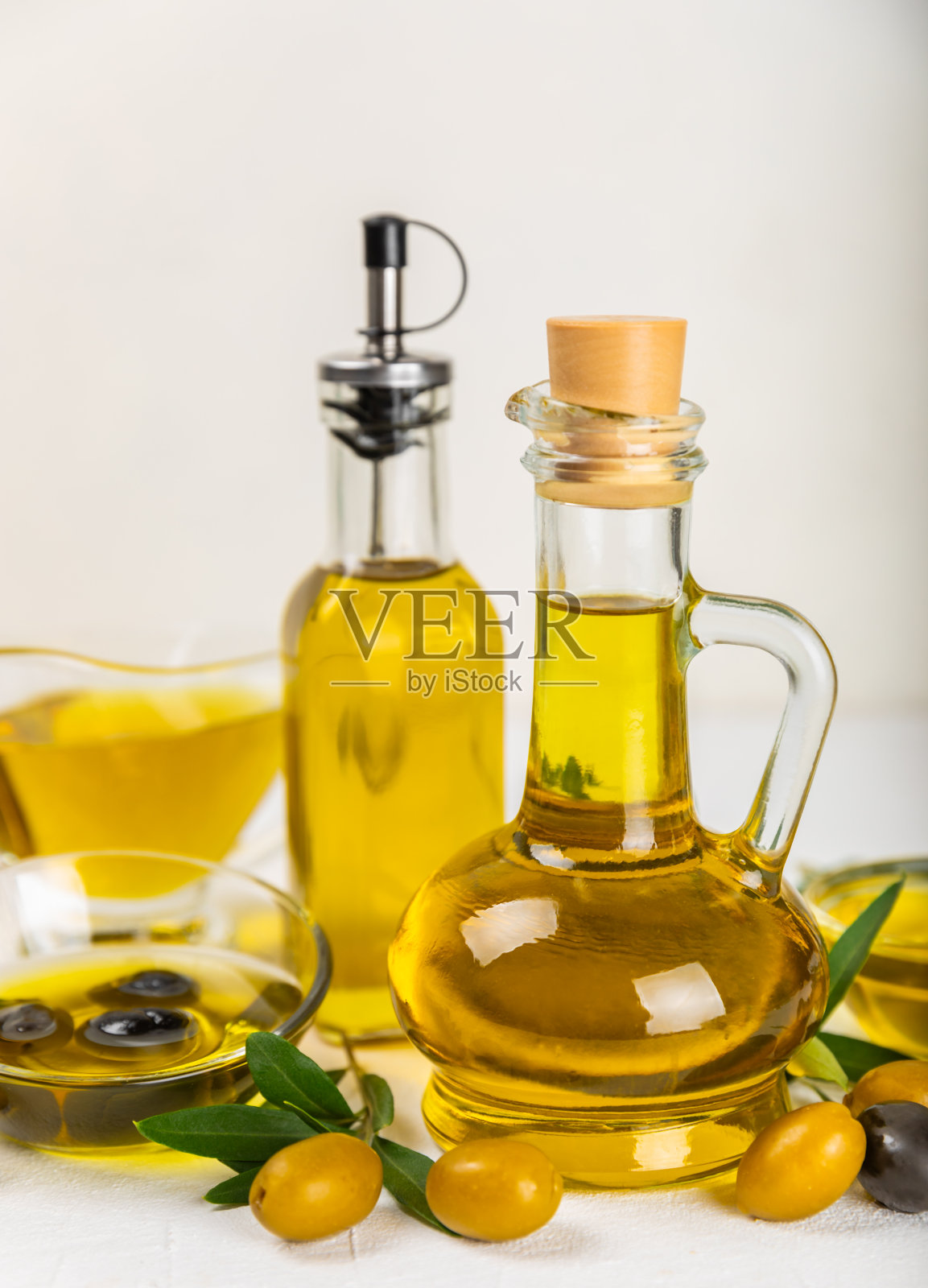 白色纹理背景上的一瓶橄榄油。油瓶上有树枝和橄榄果实。放文字的地方。副本的空间。食用油和沙拉酱。照片摄影图片
