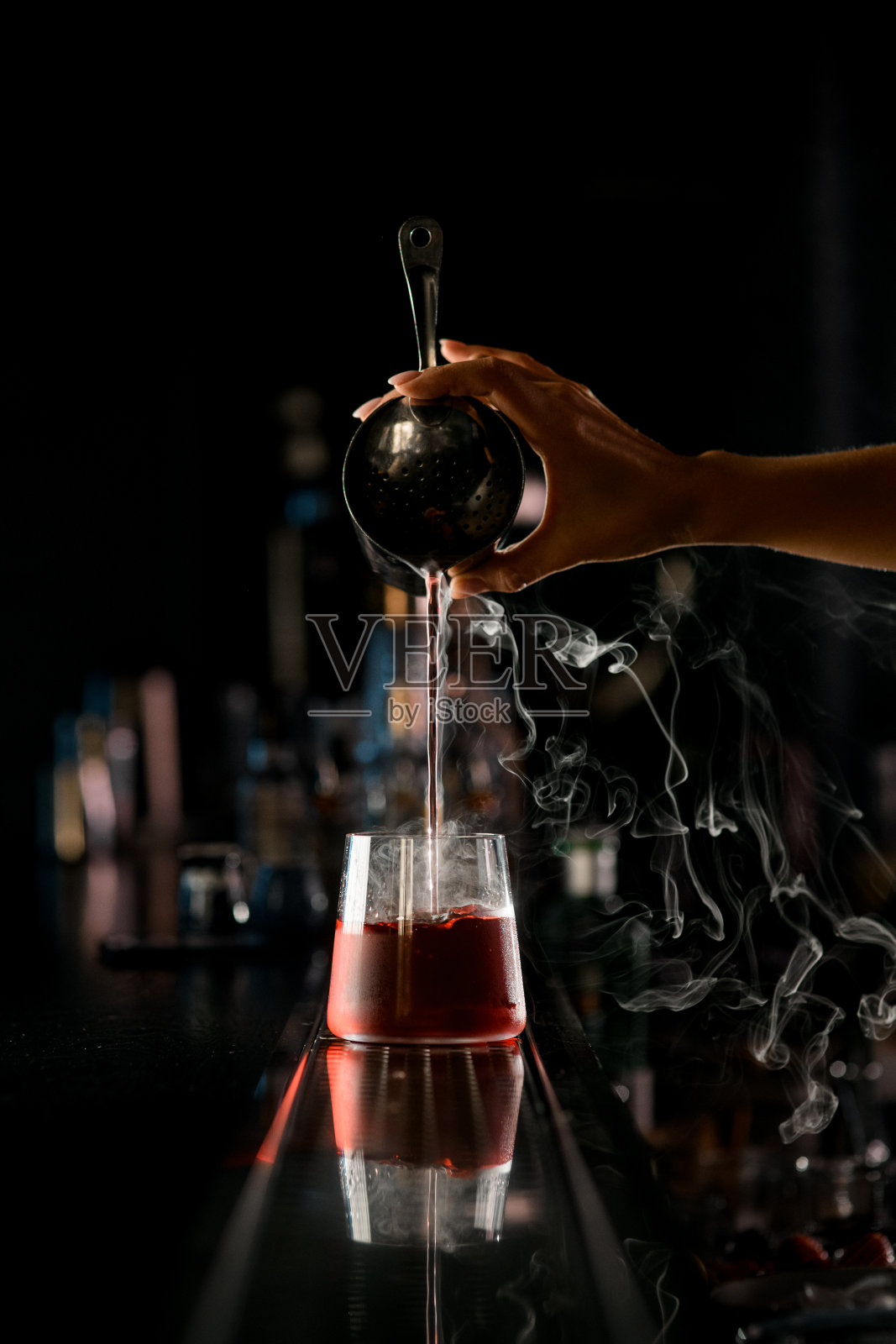 女调酒师手里的眼光准确地将钢瓶里冒着热气的液体用冰块倒进酒杯里照片摄影图片