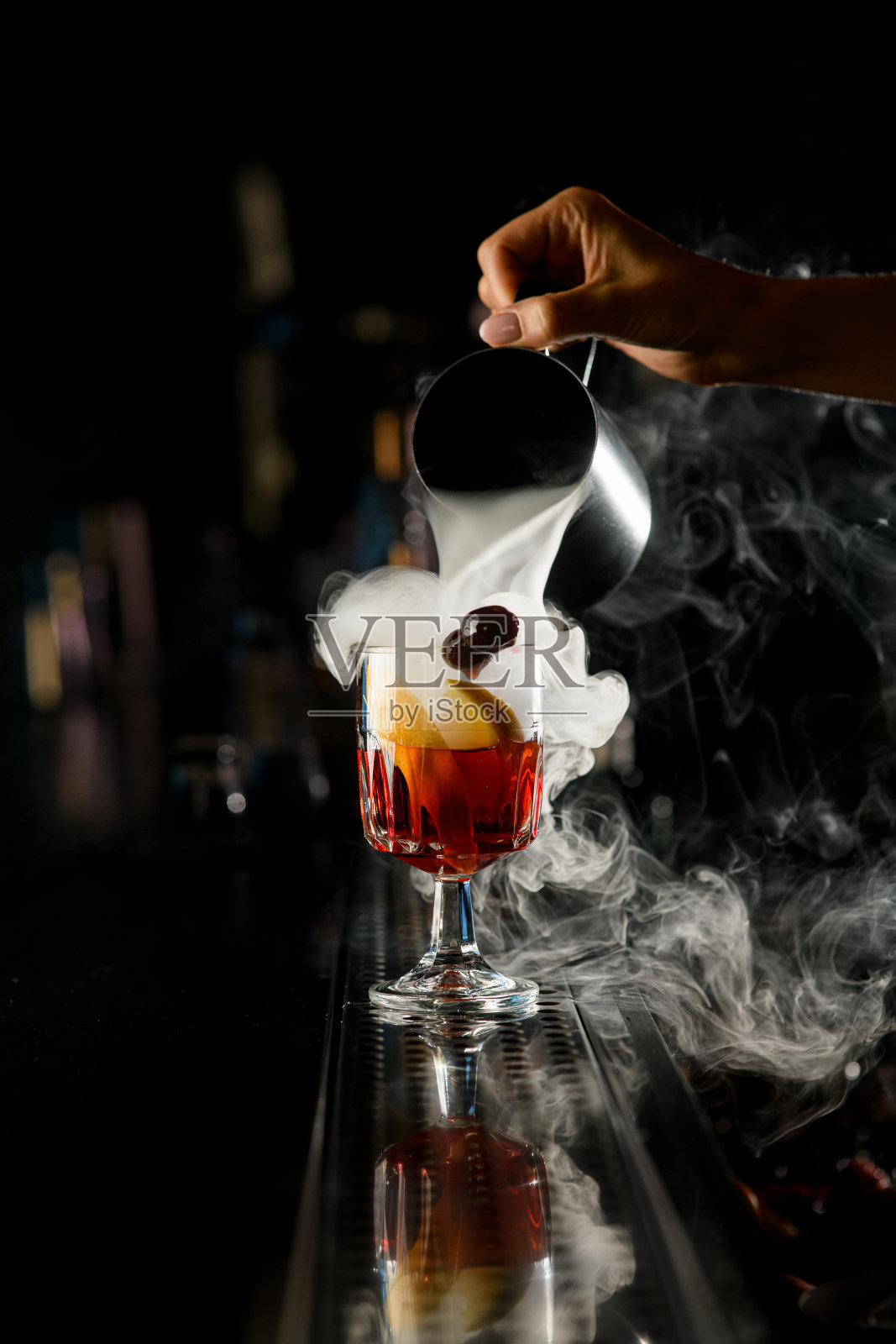 女调酒师的手将热气腾腾的鸡尾酒从钢摇杯倒进酒杯照片摄影图片