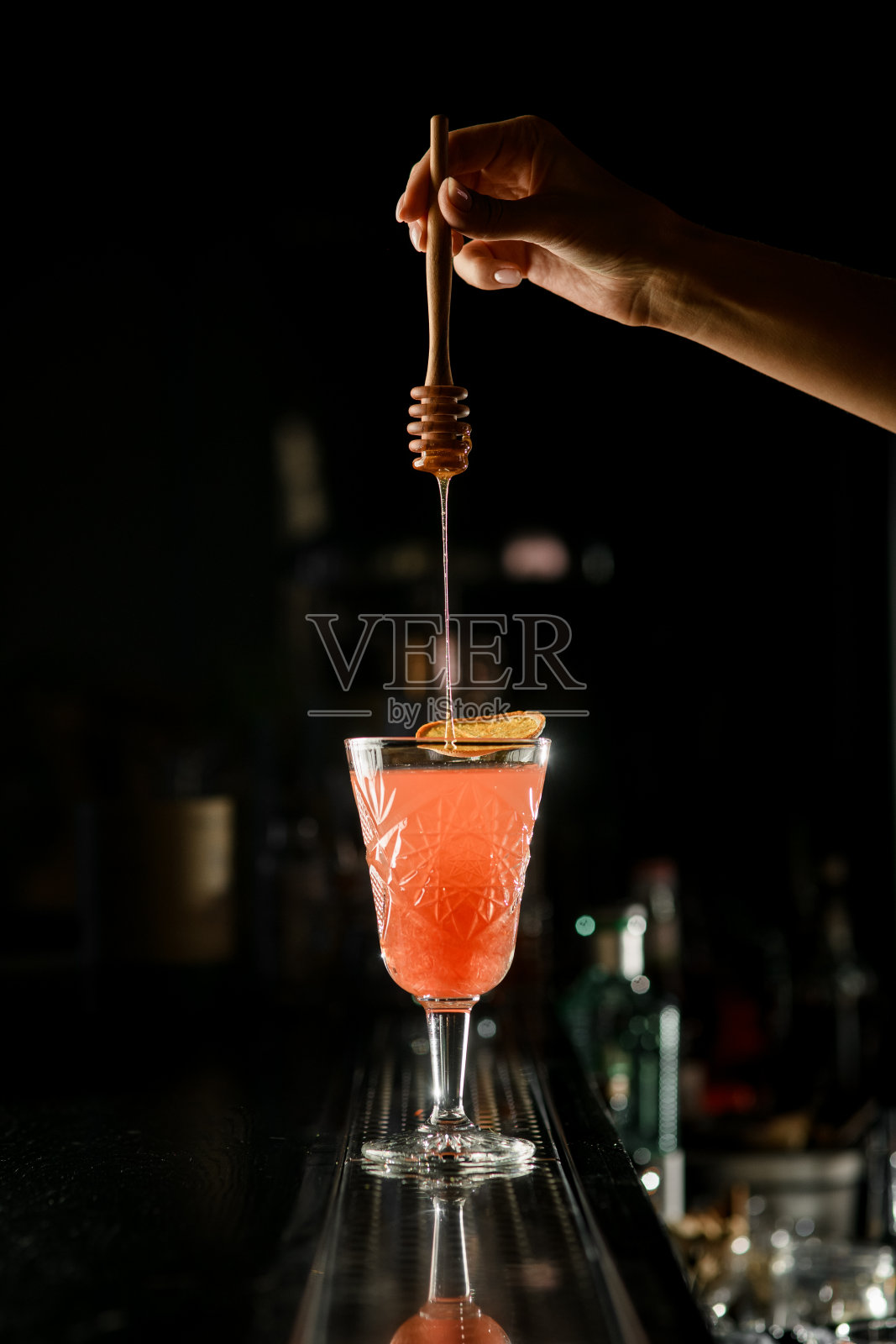 女调酒师的手拿着木勺，往老式的葡萄柚鸡尾酒酒杯里加蜂蜜照片摄影图片