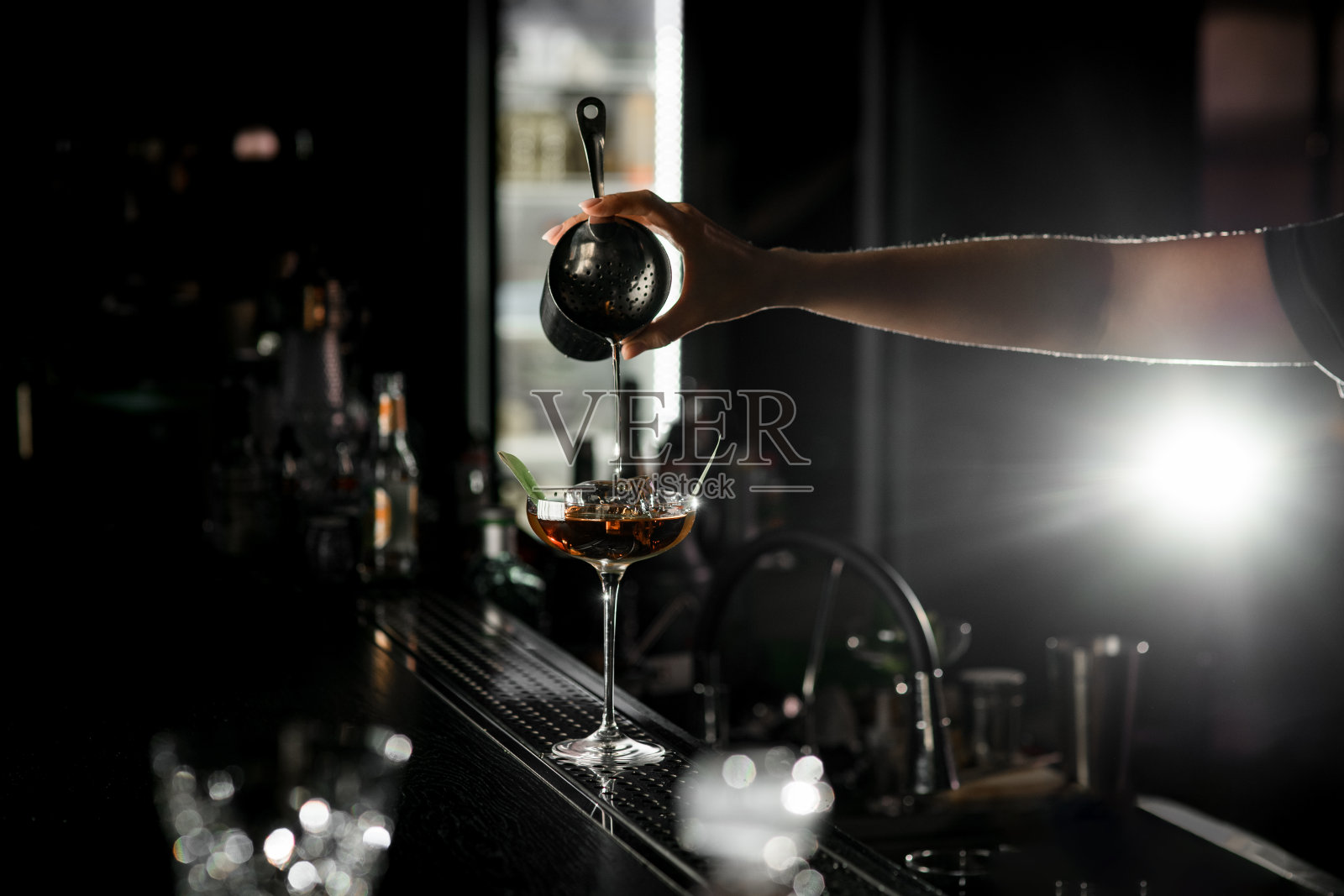 吧台上的透明马提尼酒杯，女调酒师从钢摇杯里倒酒照片摄影图片