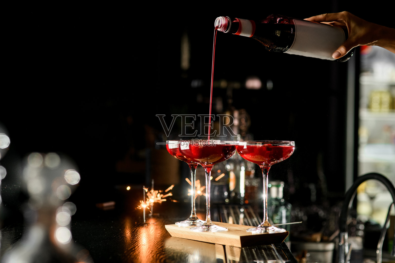 女调酒师的手拿着一瓶浆果糖浆，把它倒入马提尼杯中照片摄影图片