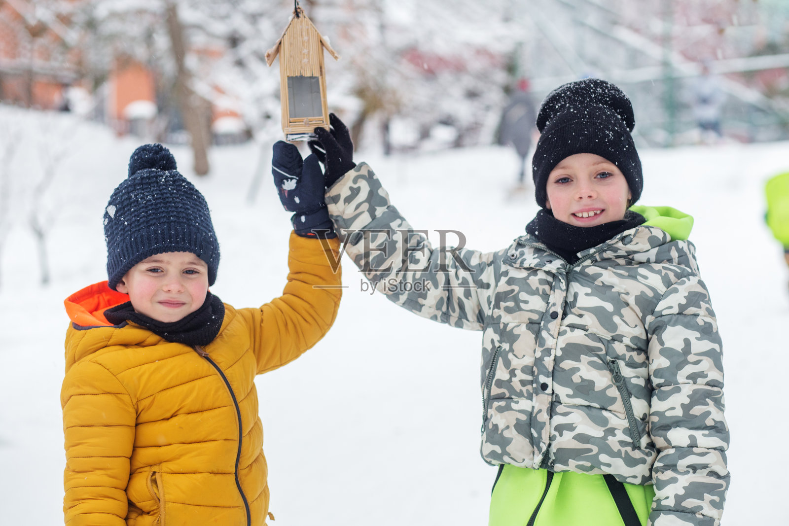 孩子们在冬天喂鸟。在白雪皑皑的花园里喂鸟。冬天的时间。寒冷的温度。照片摄影图片