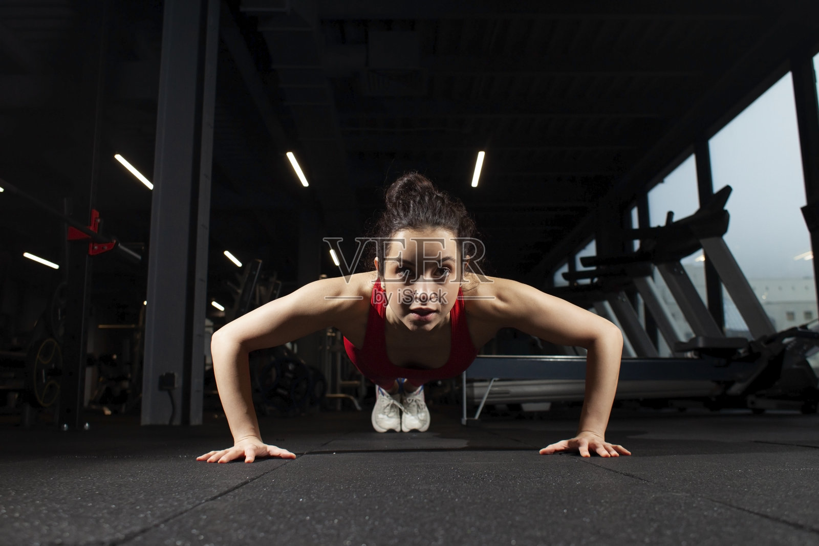 穿着红色运动服在黑色健身房训练的运动女子，在健身房做俯卧撑的女孩，迷人的强壮女子照片摄影图片