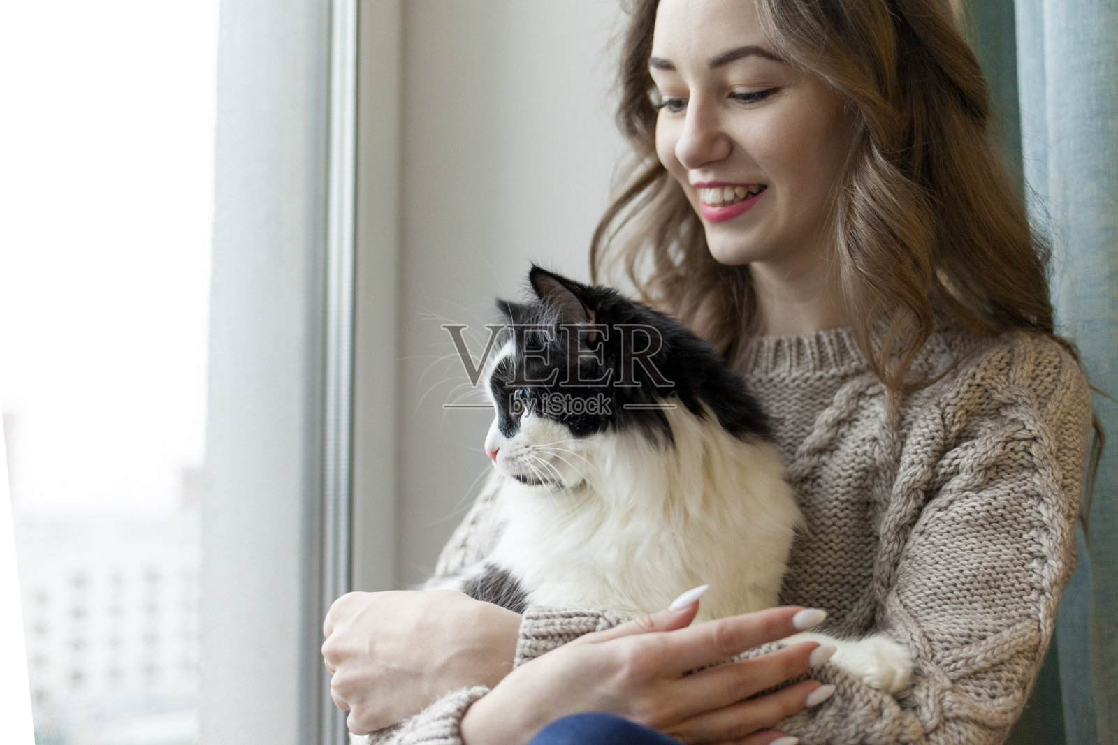 小女孩抱着黑白相间的猫坐在窗前，女人抱着宠物，看着窗外照片摄影图片