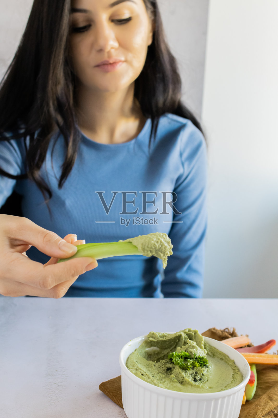 美丽的女人正在吃健康的自制奶油鹰嘴豆泥，上面有橄榄油和欧芹。用新鲜蔬菜装饰的美味素食。照片摄影图片