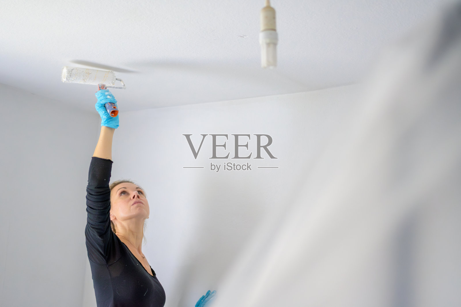 金发单身女人正在用一个大油漆滚筒粉刷她公寓的天花板照片摄影图片