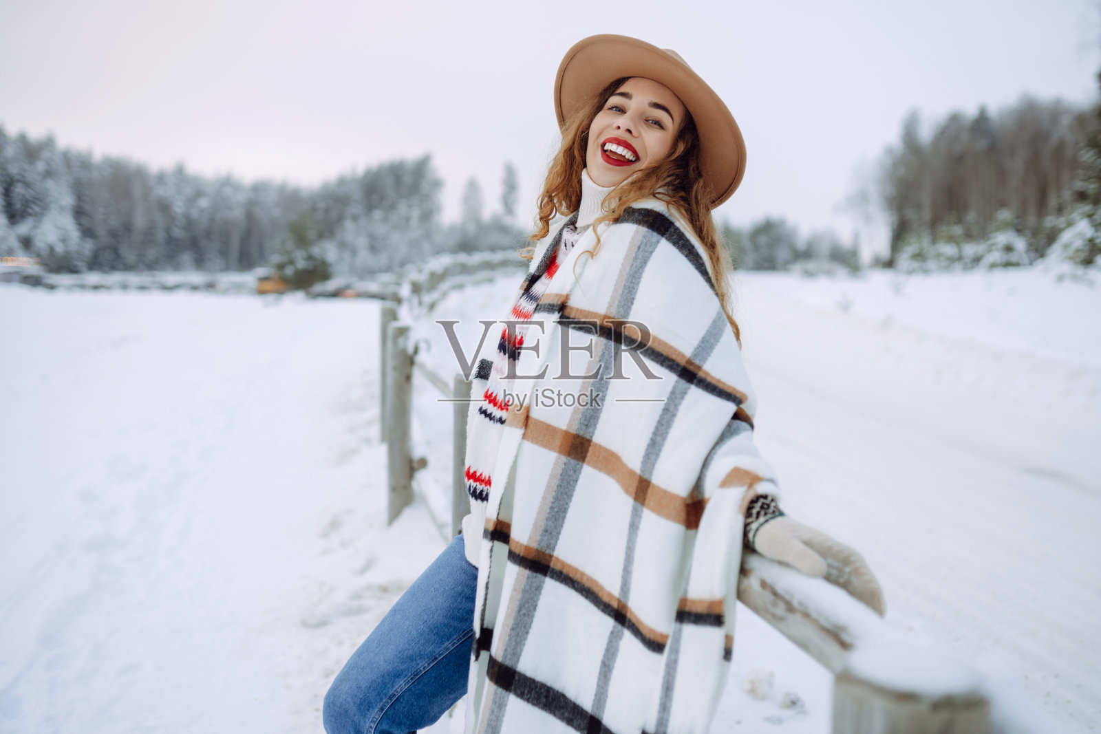 一位戴着帽子、围着围巾、在雪地里享受冬日时光的微笑女子的肖像。照片摄影图片