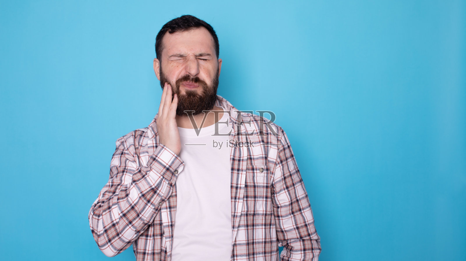 不健康的大胡子男人的肖像，压迫疼痛的脸颊，患有急性牙痛，牙周病，蛀牙或下颌疼痛。照片摄影图片