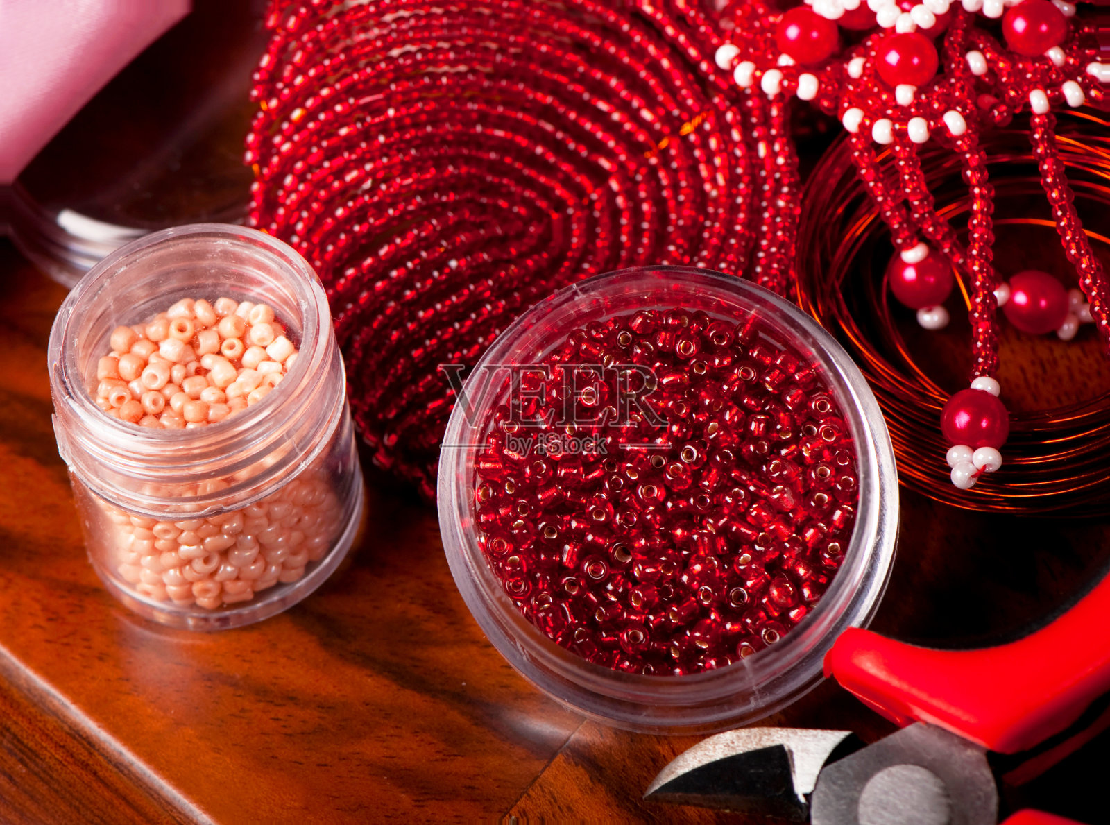 制作手工首饰的工具。旧木背景上有红色珠子的盒子。手工制作的配件。从上面看照片摄影图片