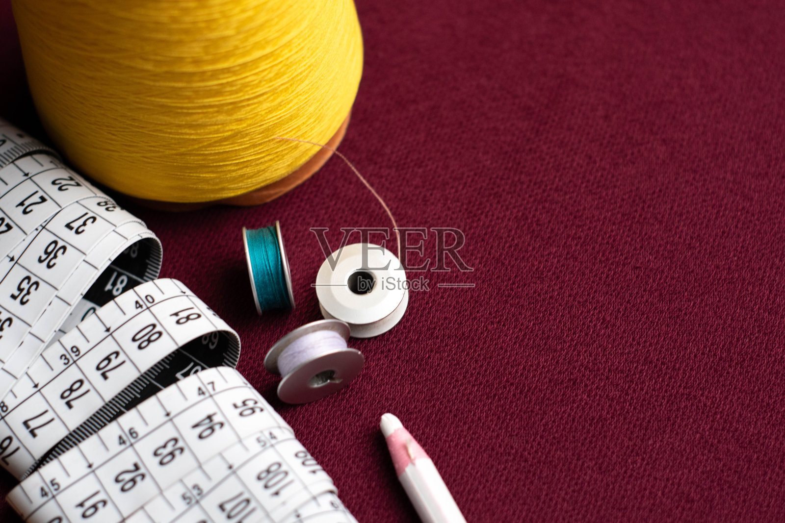 塑料白色的米，黄色的线锥和线轴在具有纺织质感的暗红色织物上照片摄影图片
