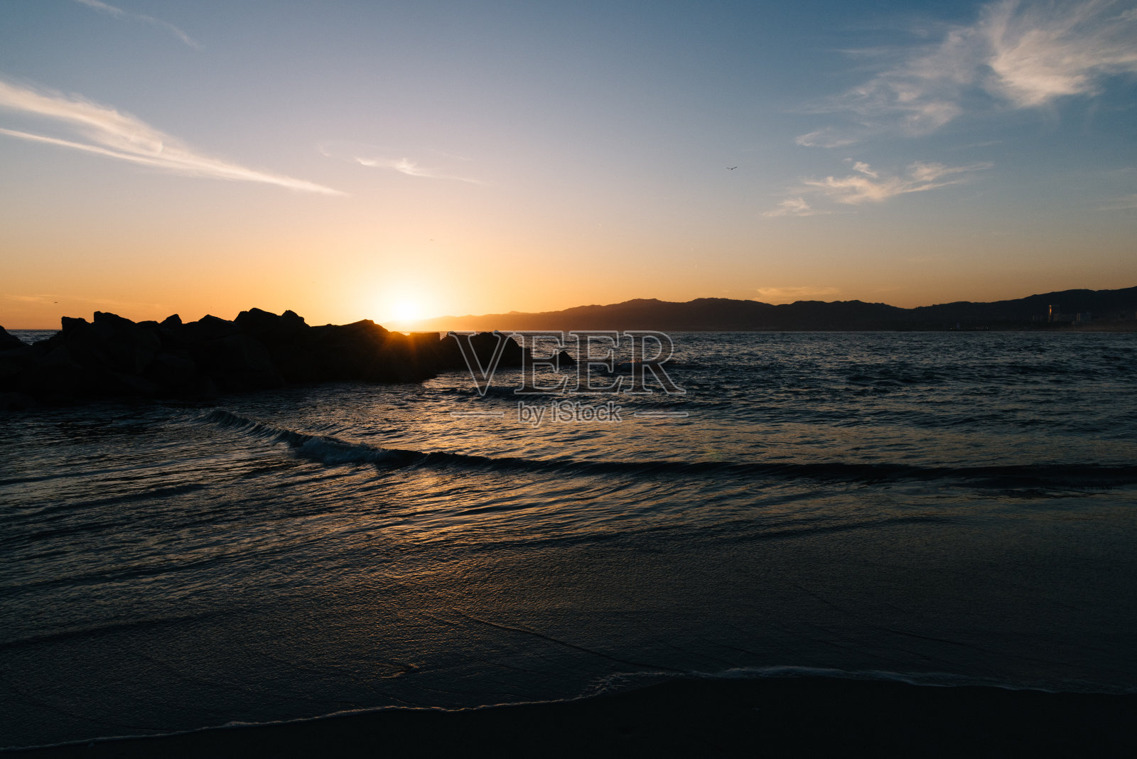 海滩上岩石后面的夕阳照片摄影图片