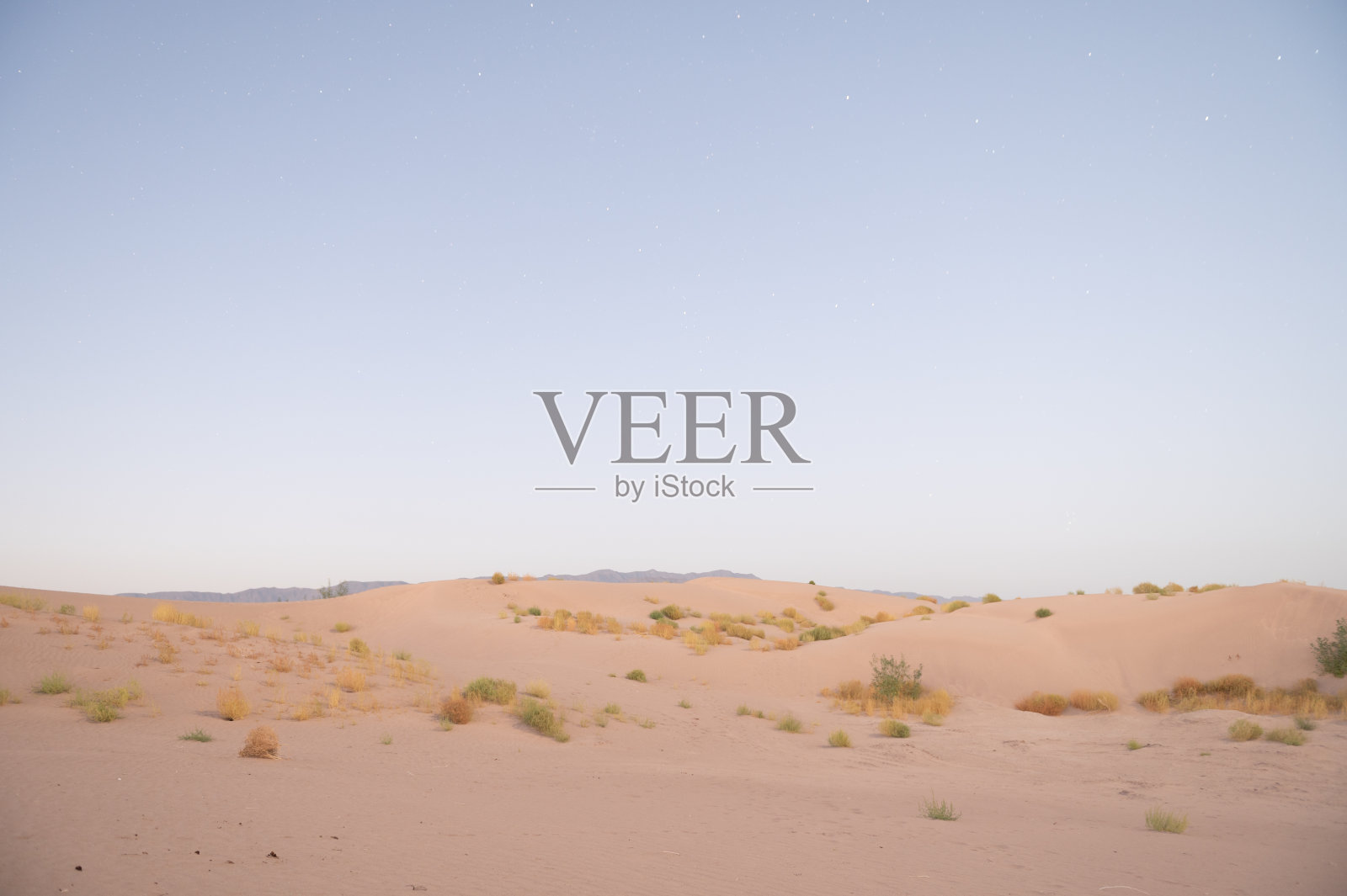 日落时令人惊叹的景观，沙漠中间的沙丘在沙子中有阴影，绿色的小植被，山脉和广阔的沙漠是区分开来的。照片摄影图片