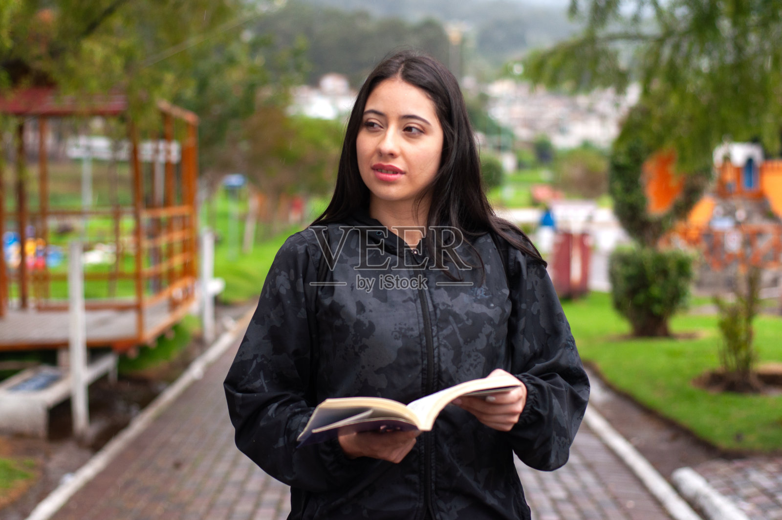 迷人的年轻拉丁人在公园散步，手里拿着一本书，在早晨散步时看着旁边。书的一天照片摄影图片