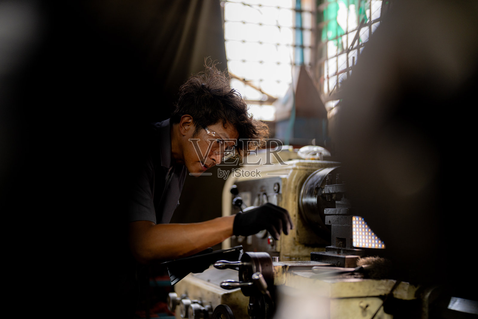 生产厂的亚洲工人在机器上钻孔。工厂内钻床附近的专业工人。在车床磨床上用飞溅的火花完成金属加工的内钢表面。照片摄影图片