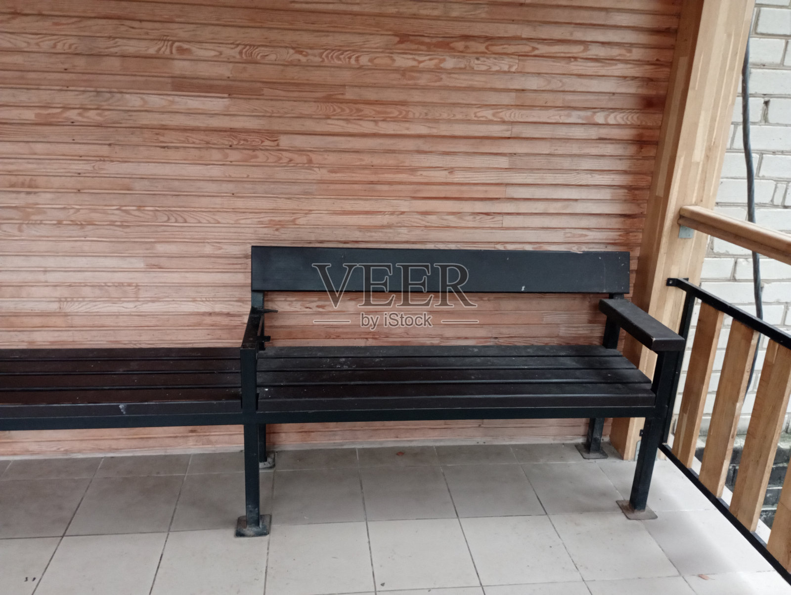 阳台上靠近隔板墙的黑色靠背长凳。休闲区有一个木凳在掩护下。照片摄影图片