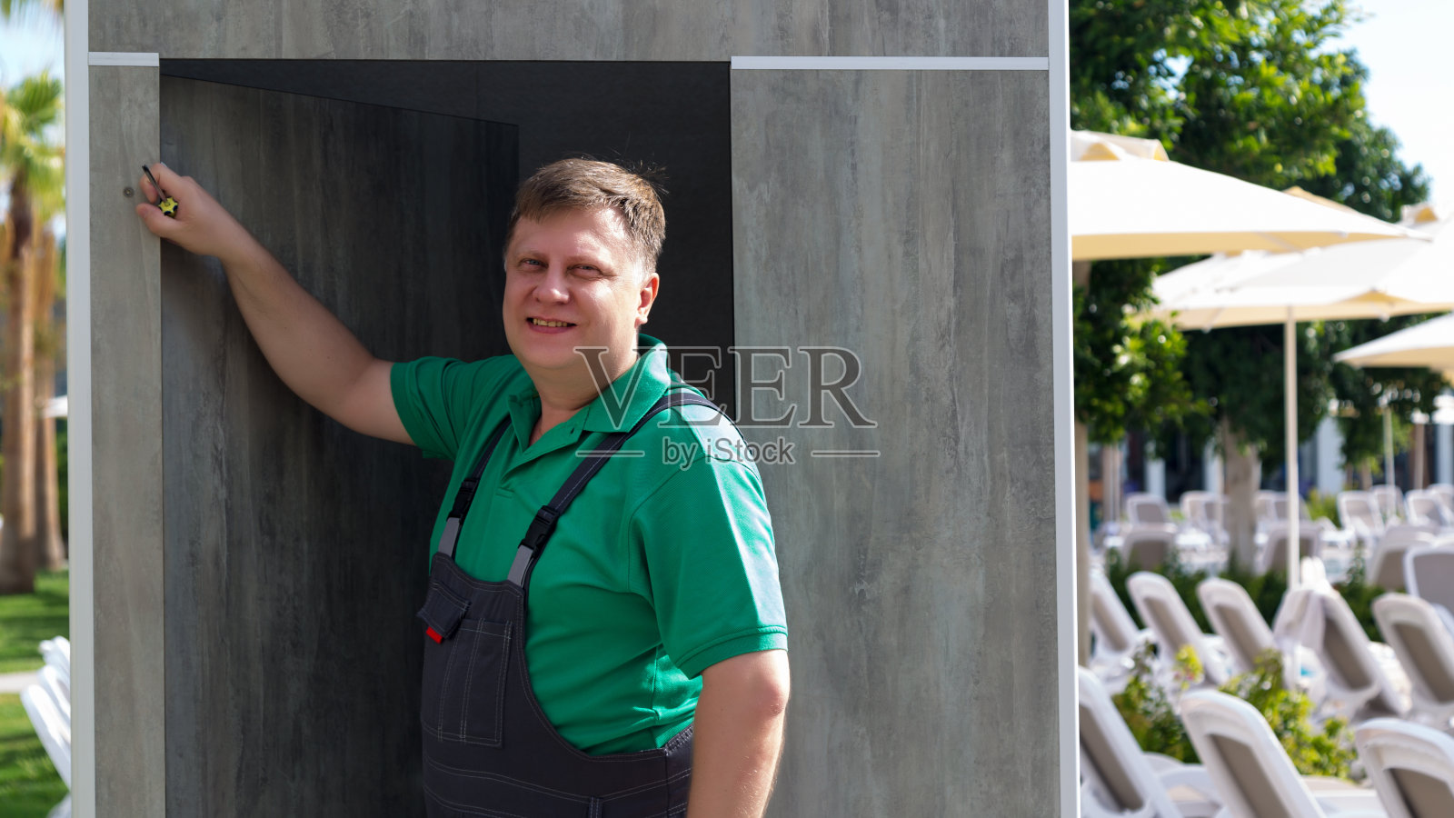 宾馆里的一名工人正在修理游泳池附近的更衣室，正在拧衣钩照片摄影图片