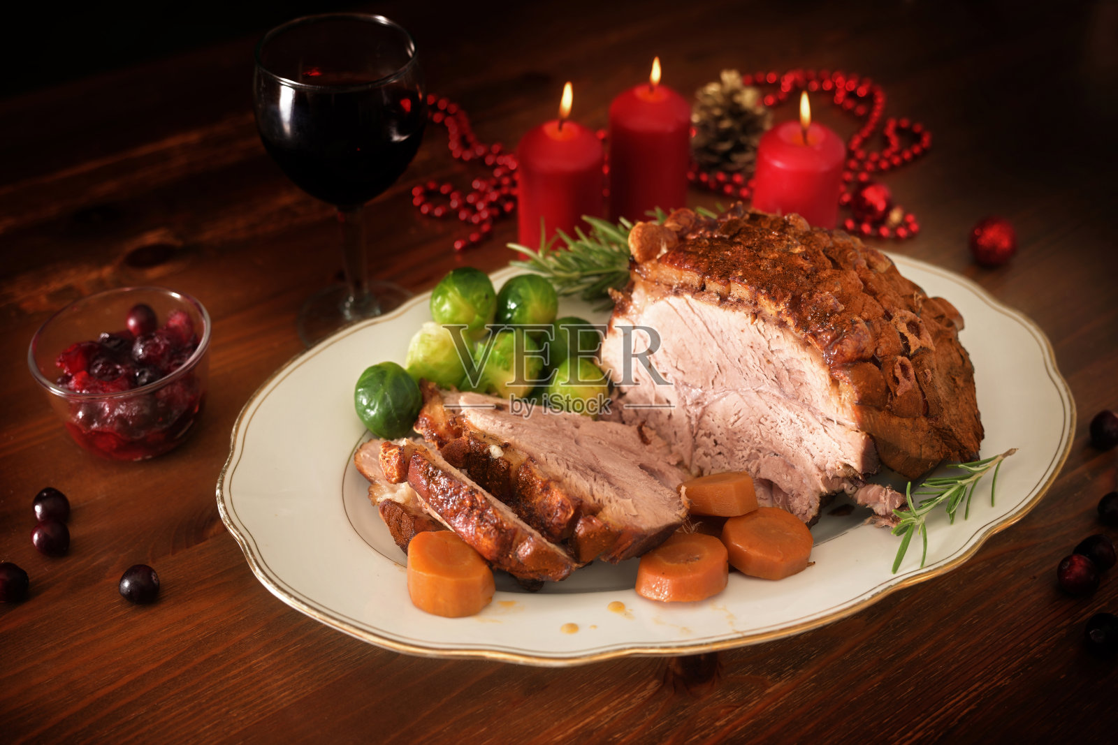 烤猪肉或带皮的圣诞火腿，配上蔬菜和蔓越莓，放在深色的木桌上，点着蜡烛，复制空间，选择重点照片摄影图片